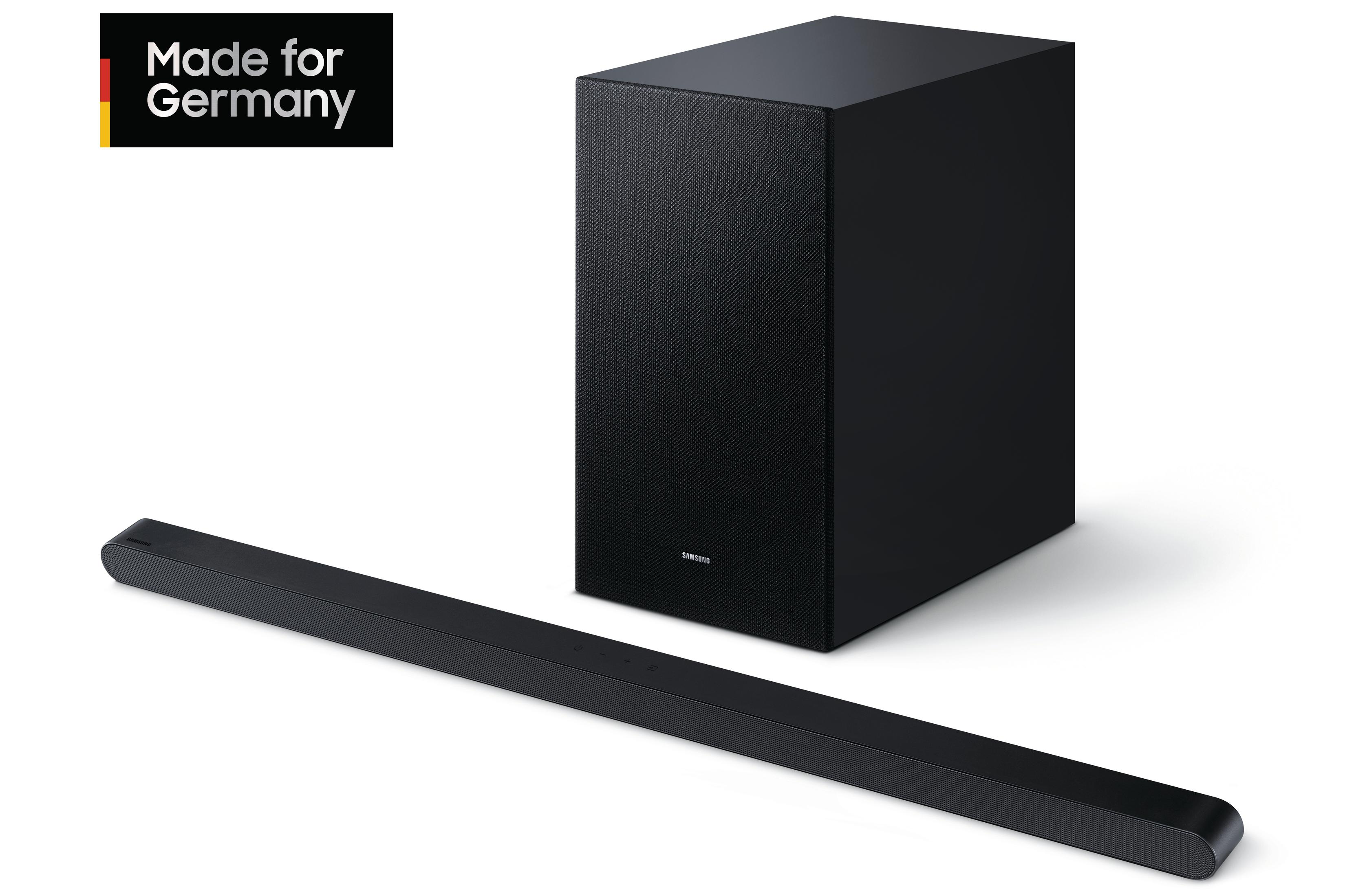 Eine schwarze Soundbar und ein schwarzer Subwoofer. Das Setup befindet sich auf einer weißen Oberfläche. Text sagt Made for Germany.
