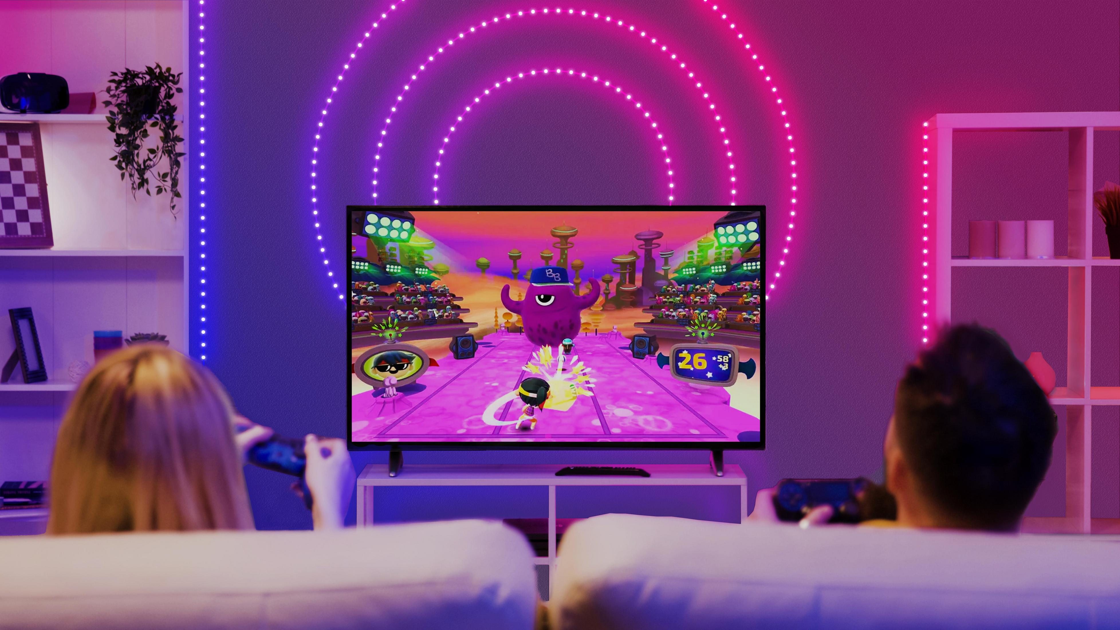 Dwie osoby grają w grę wideo na telewizorze. Pokój jest ciemny z neonami.