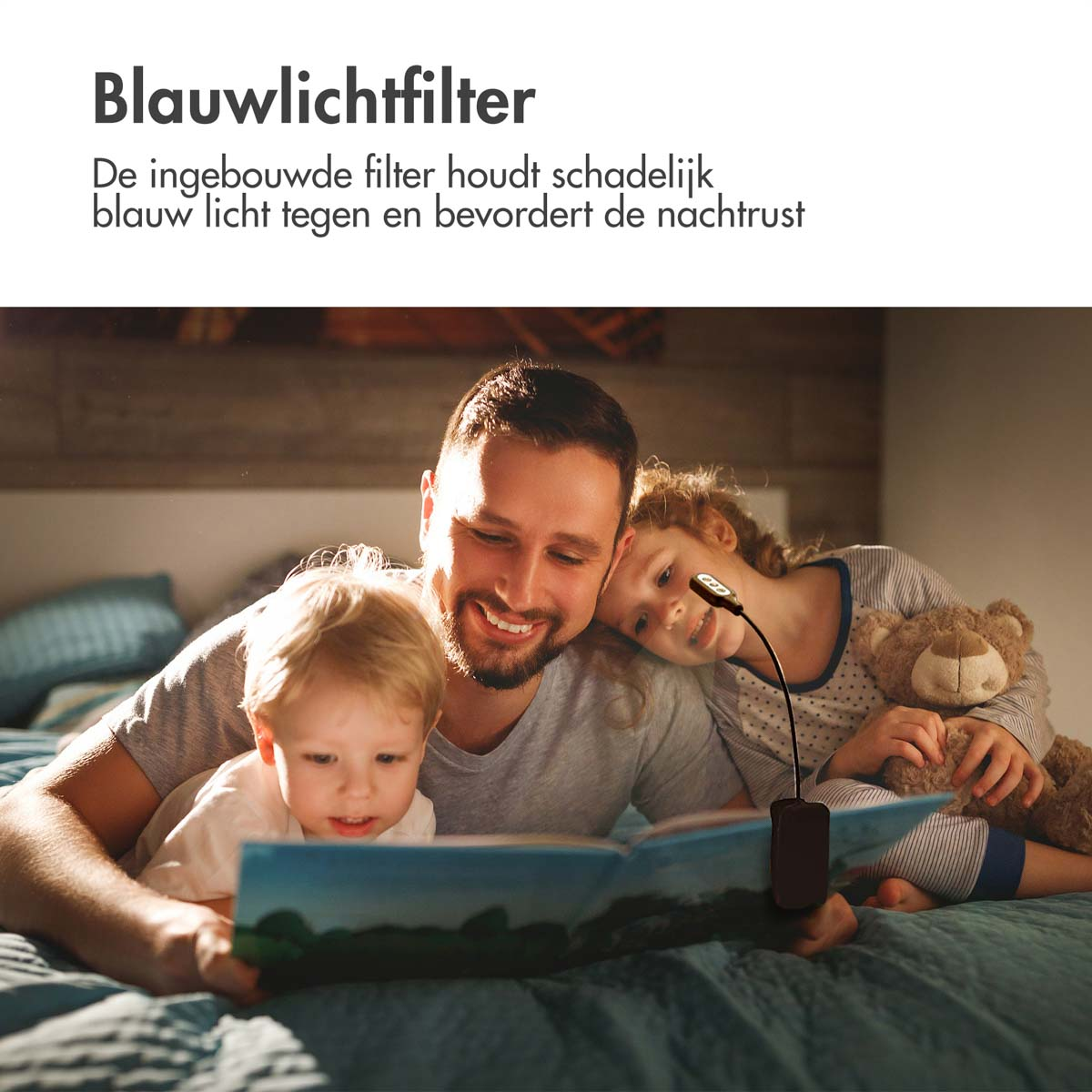 A family reading a book in bed with a small lamp. A toddler and a girl are present, and a teddy bear is on the bed.