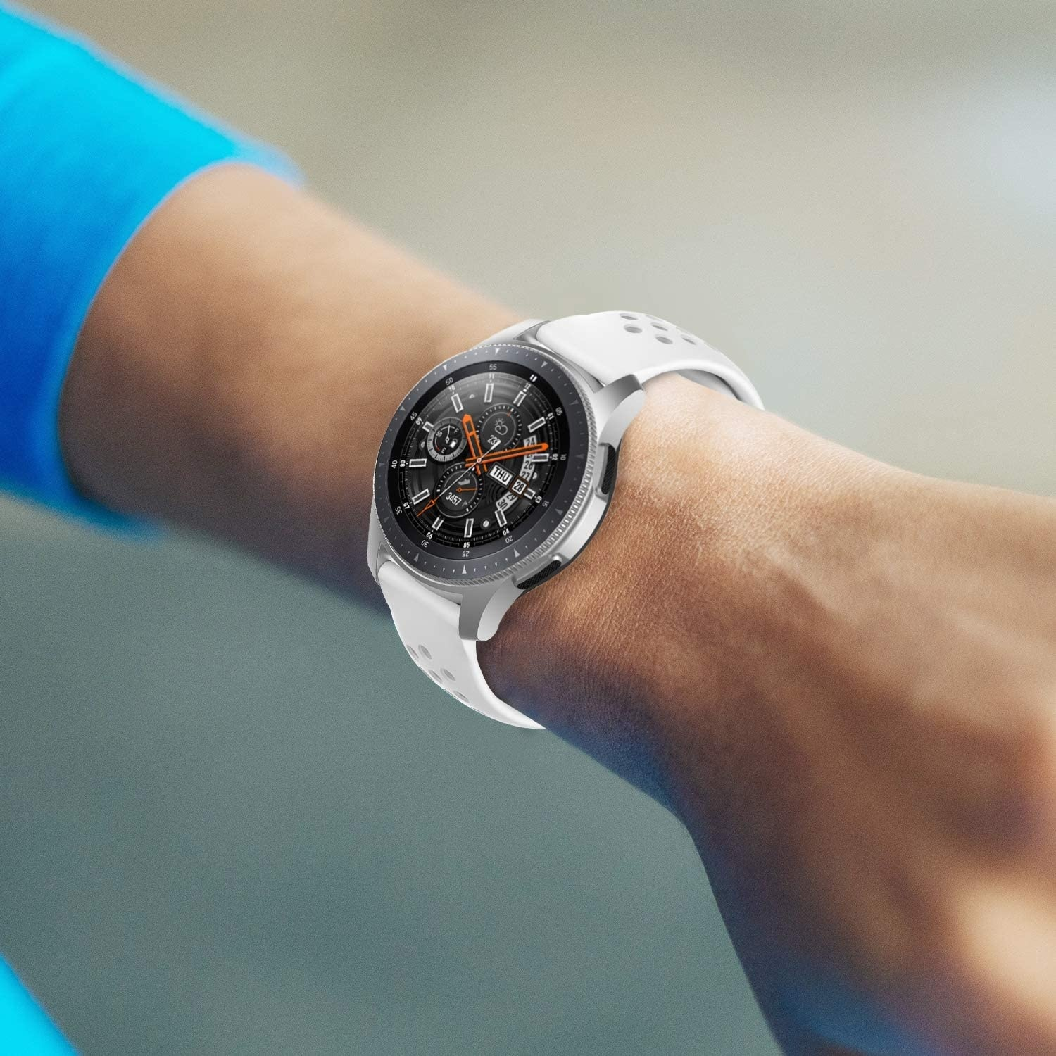Das Handgelenk einer Person mit einer weißen Smartwatch. Die Uhr zeigt die Uhrzeit an. Der Hintergrund ist verschwommen.