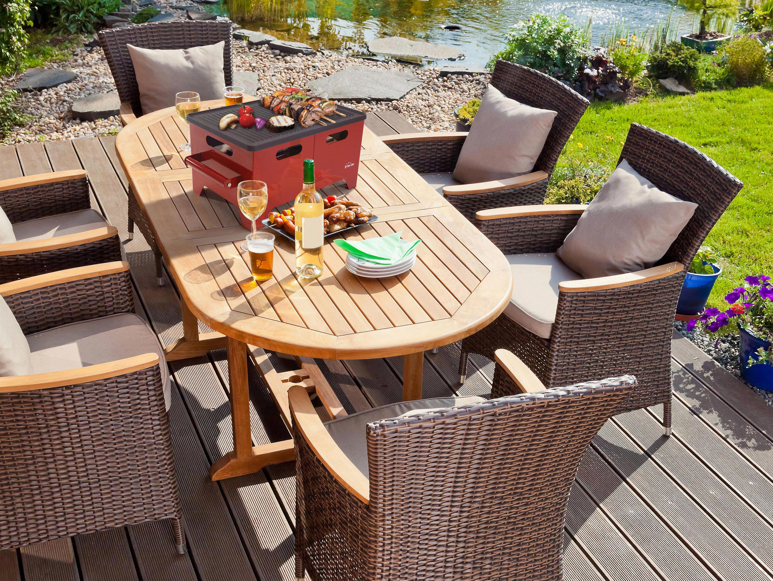 Essplatz im Freien mit rotem Grill, Tisch, Stühlen und Essen. Ein Teich im Hintergrund.