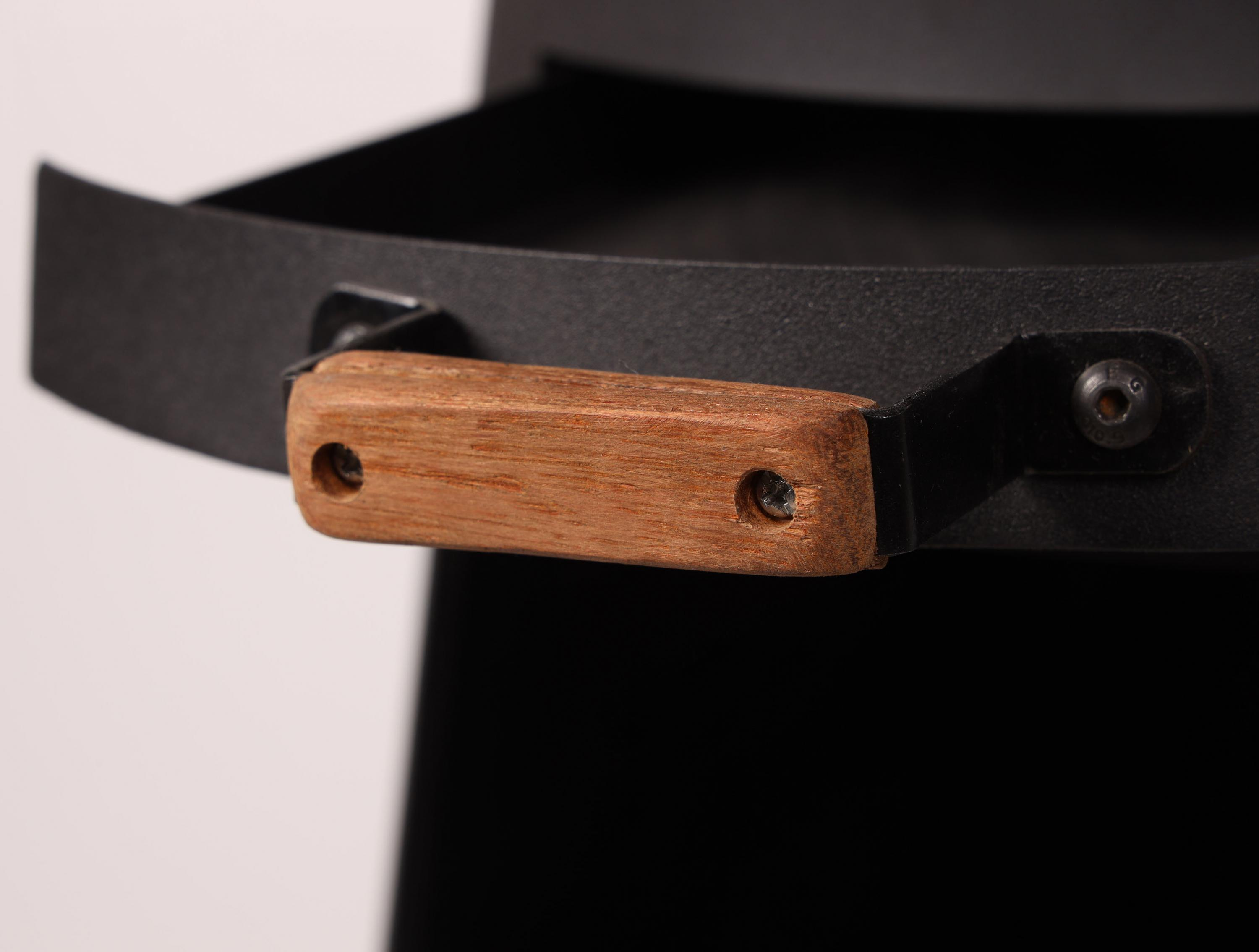 Nahaufnahme eines Holzgriffs, der an einem schwarzen Metallobjekt mit Schraubenlöchern befestigt ist.
