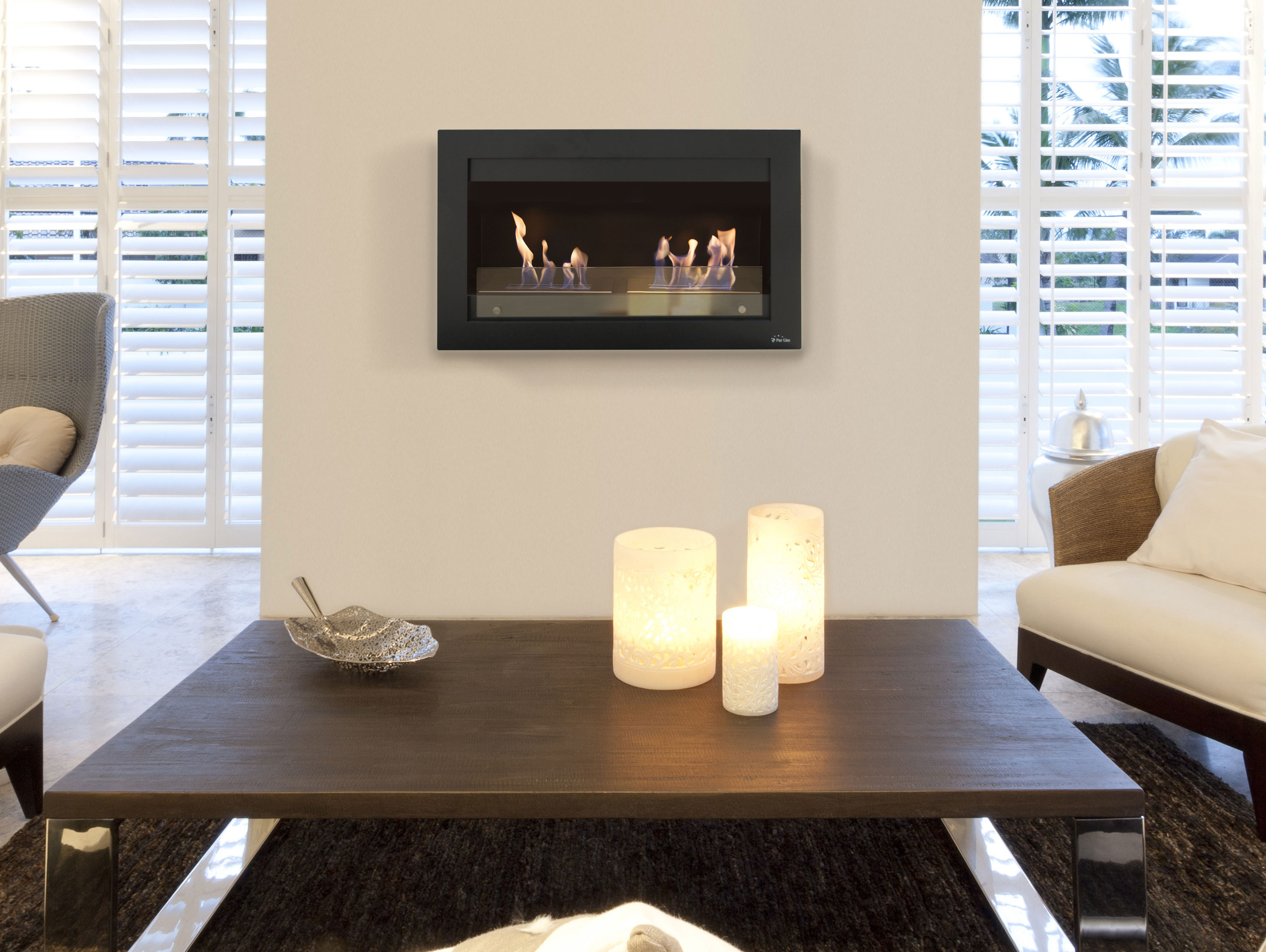 Kamin an der Wand, schwarzer Rahmen, Flammen sichtbar. Tisch mit Kerzen davor.