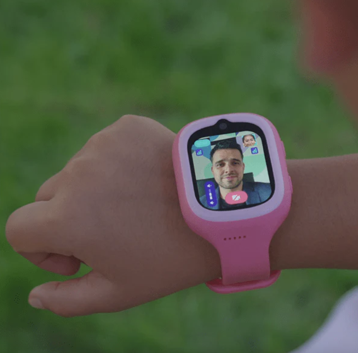 Un reloj inteligente rosa muestra una videollamada con dos personas. Está en una mano sobre fondo verde.