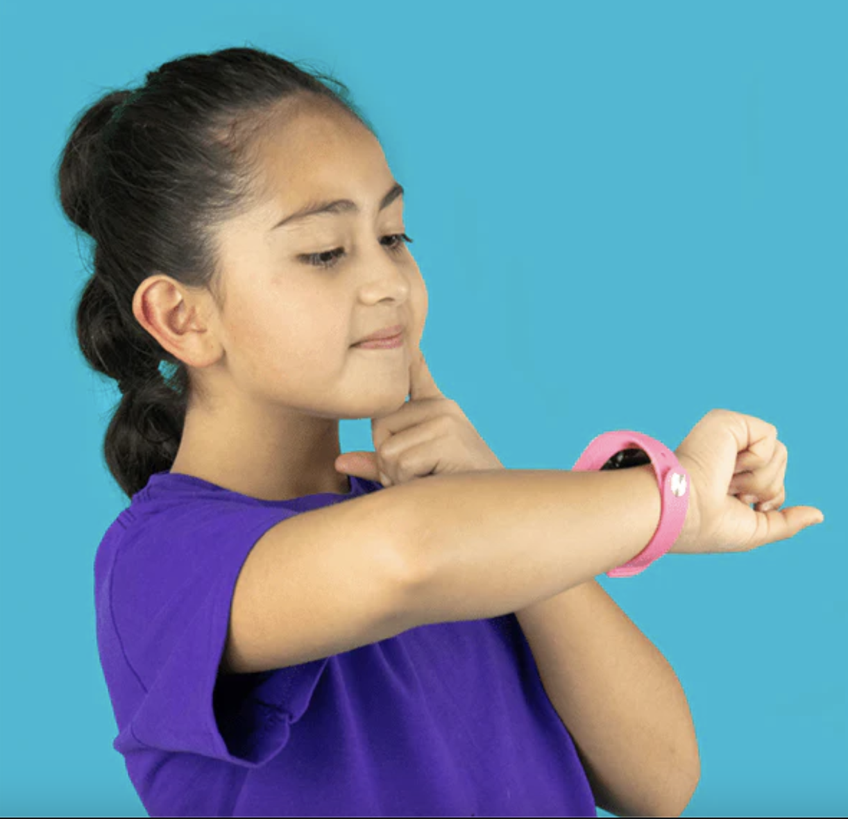Una niña con un smartwatch rosa sobre fondo azul, mirando su muñeca.