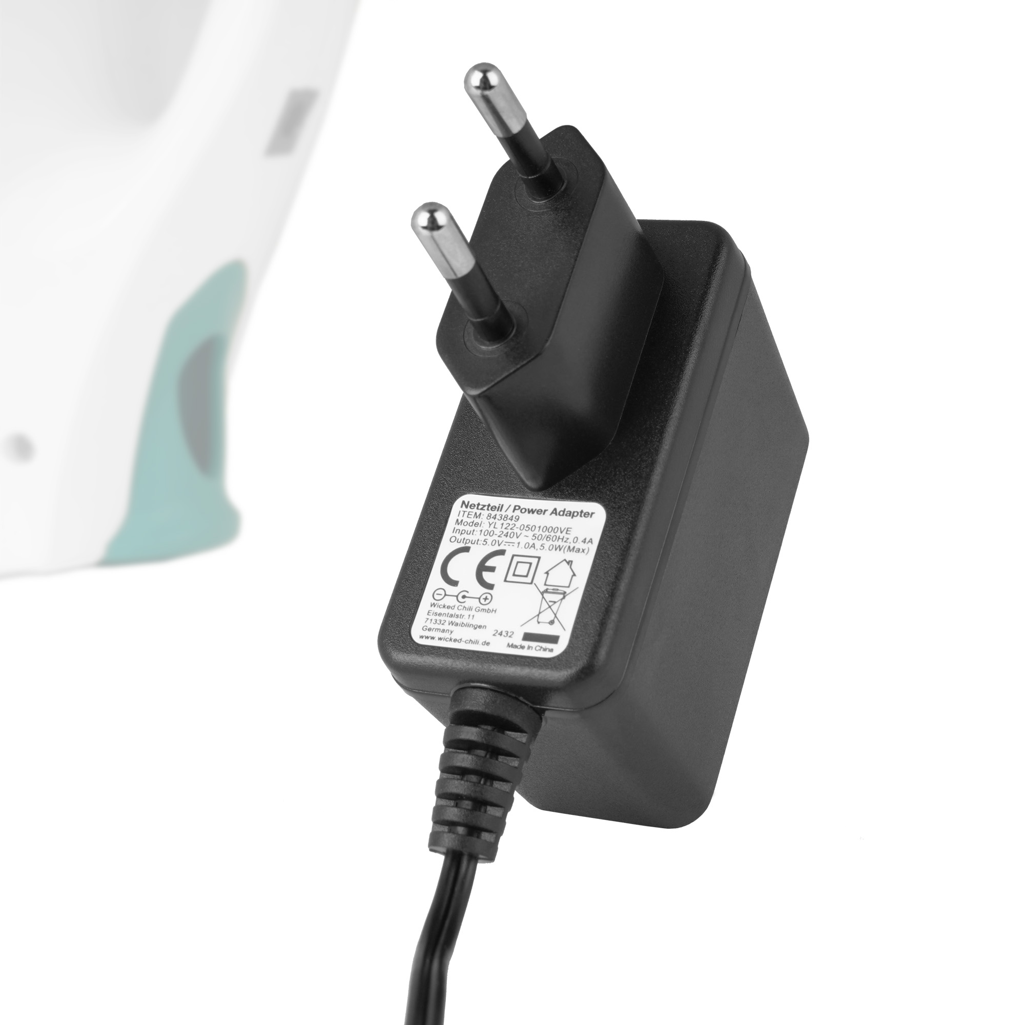Ein schwarzer Netzadapter mit Stecker, verbunden mit einem Kabel. Der Adapter befindet sich in der Nähe eines weißen und tealfarbenen Geräts.
