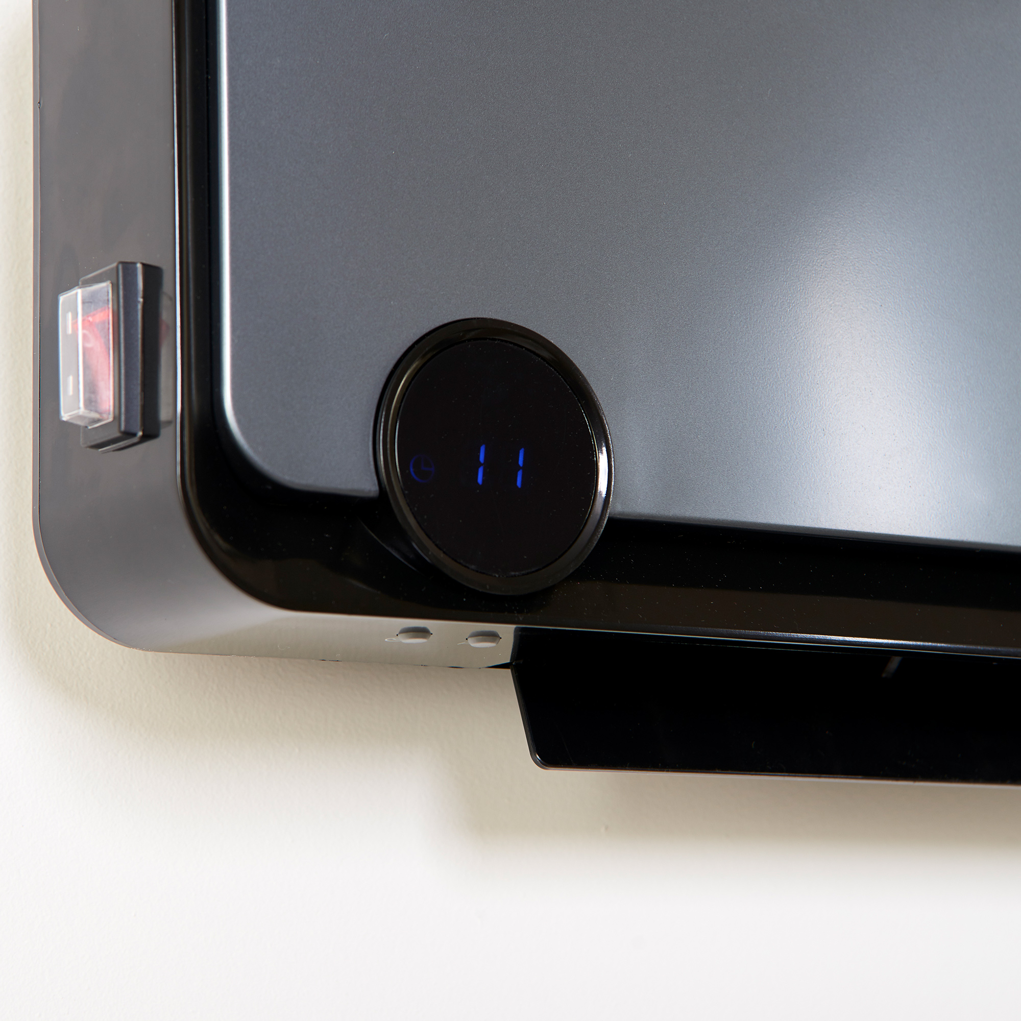 Zbliżenie na panel sterowania czarnego grzejnika elektrycznego. Ma przełącznik i wyświetlacz cyfrowy.