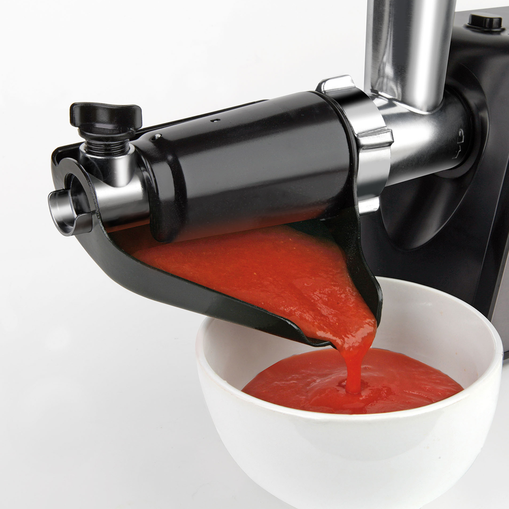 Maszynka do mięsa z sosem pomidorowym wlewanym do białej miski, białe tło, ujęcie studyjne.