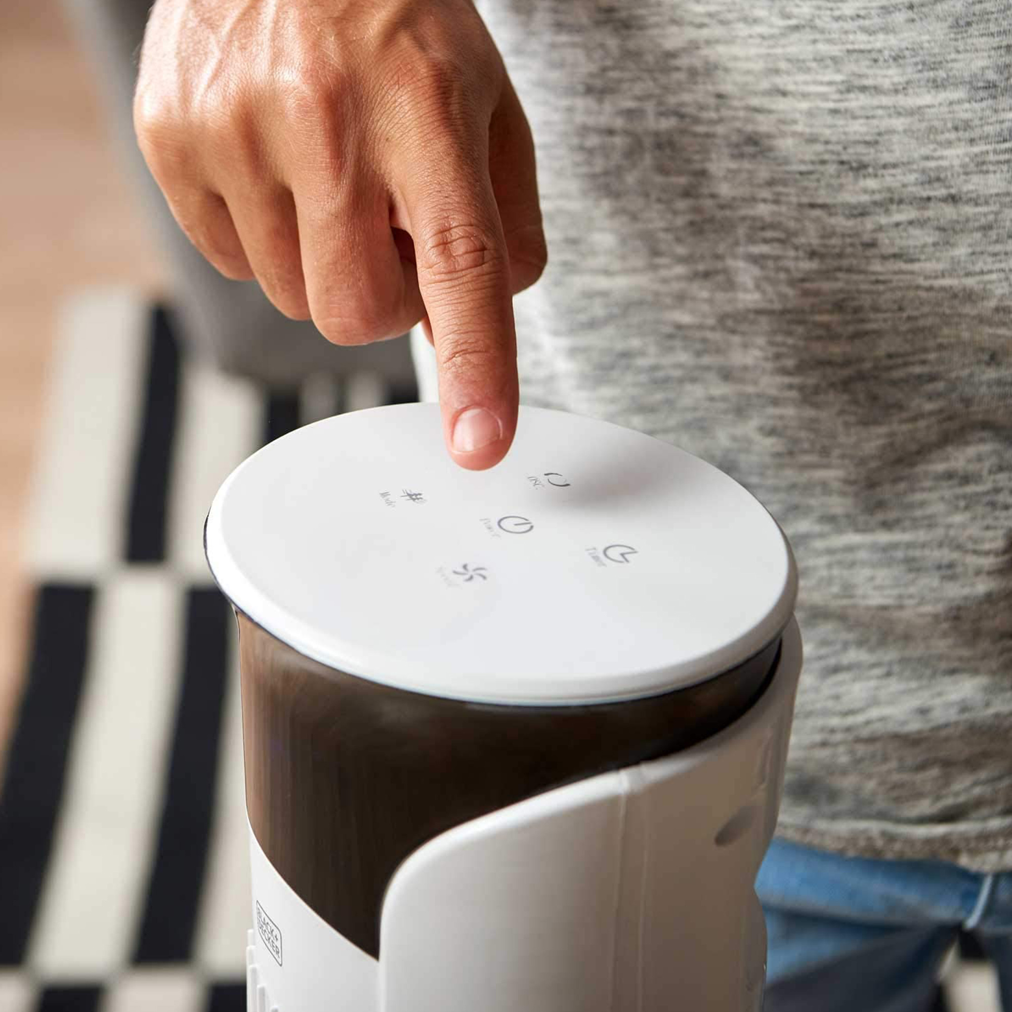 Der Finger einer Person drückt einen Knopf auf einem weißen und schwarzen Ventilator.