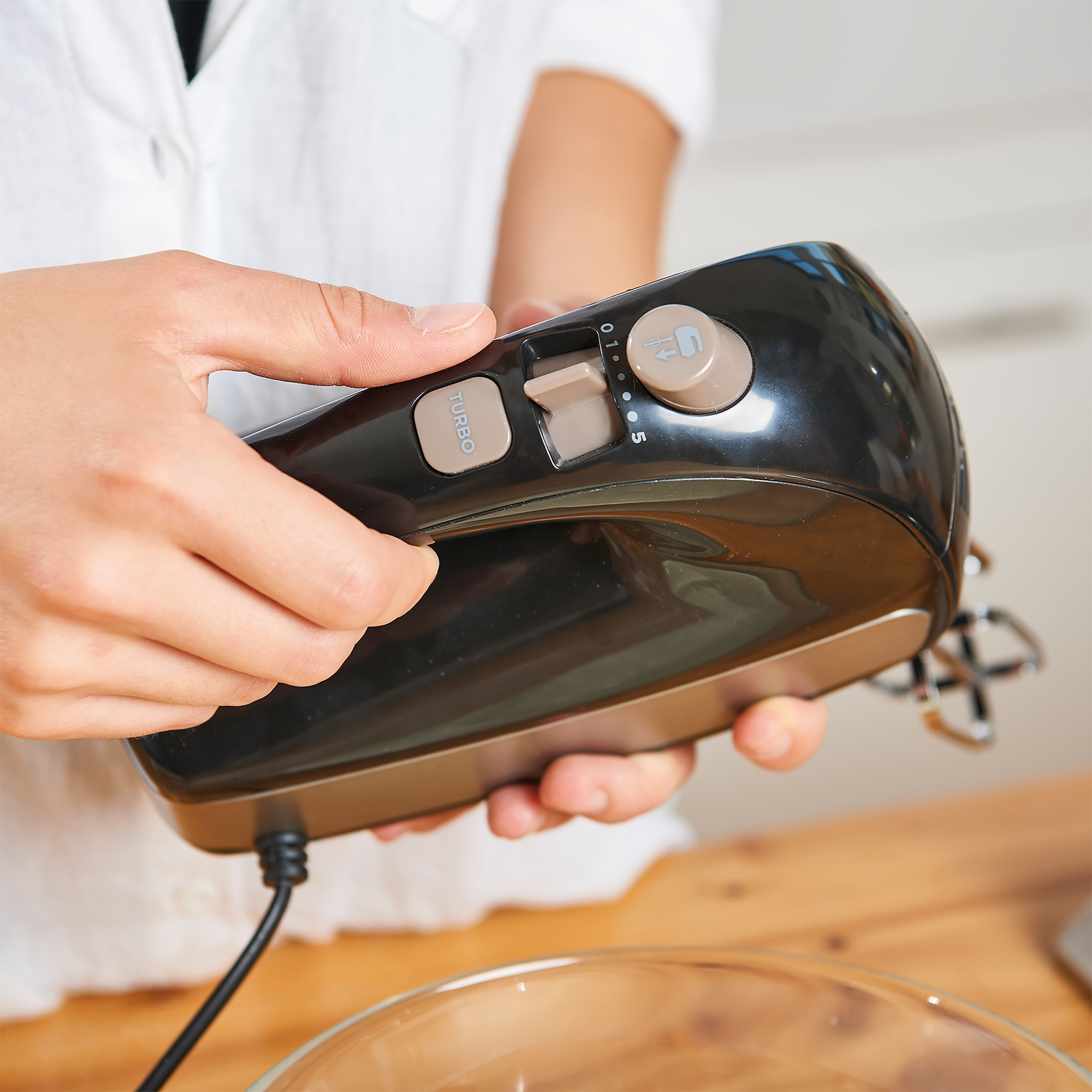 Eine Person hält einen schwarz-braunen Handmixer. Der Mixer hat eine Turbo- und Geschwindigkeitsregelung.