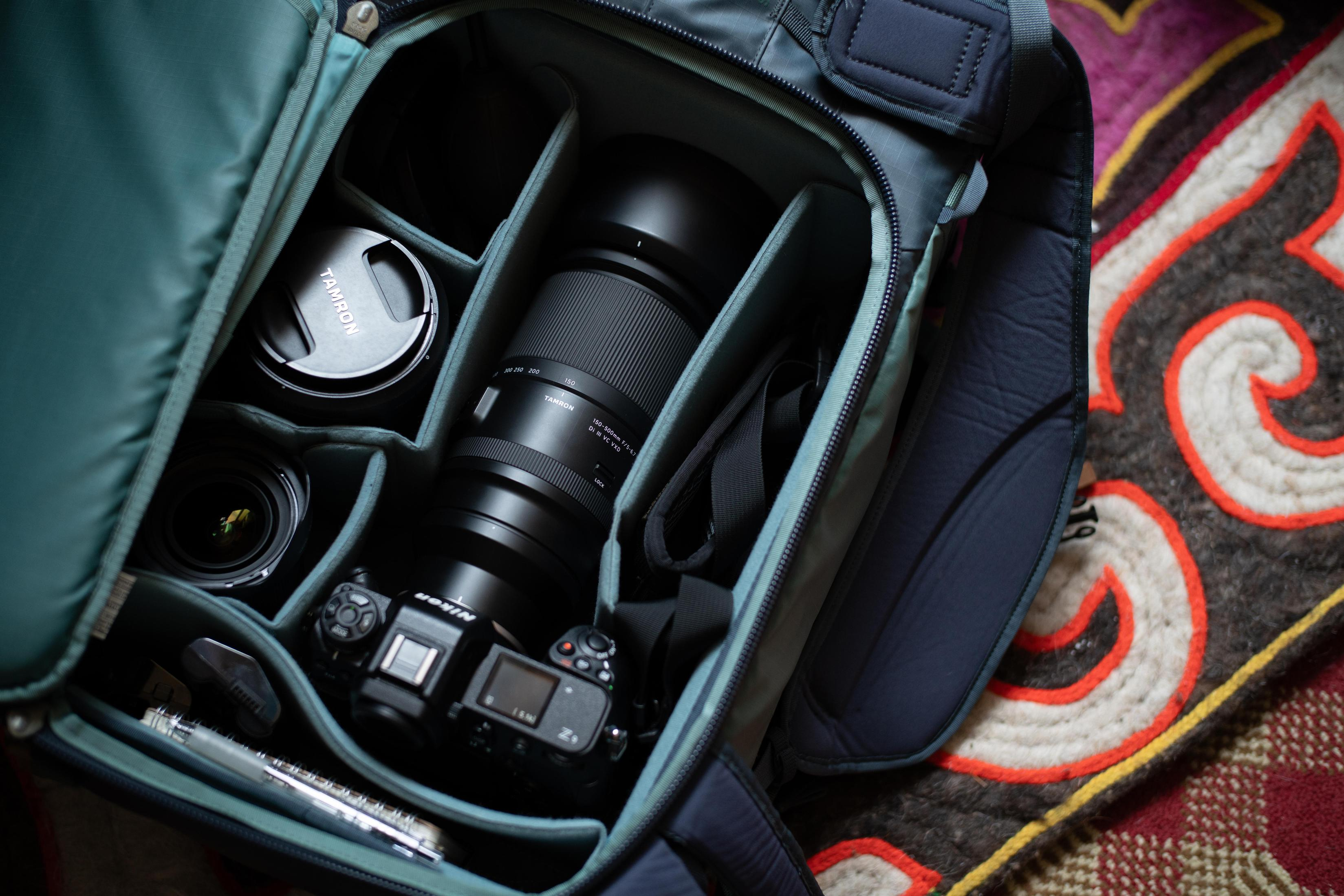 Otwarta torba na aparat z różnymi obiektywami, aparatem i akcesoriami, na tle ze wzorem.