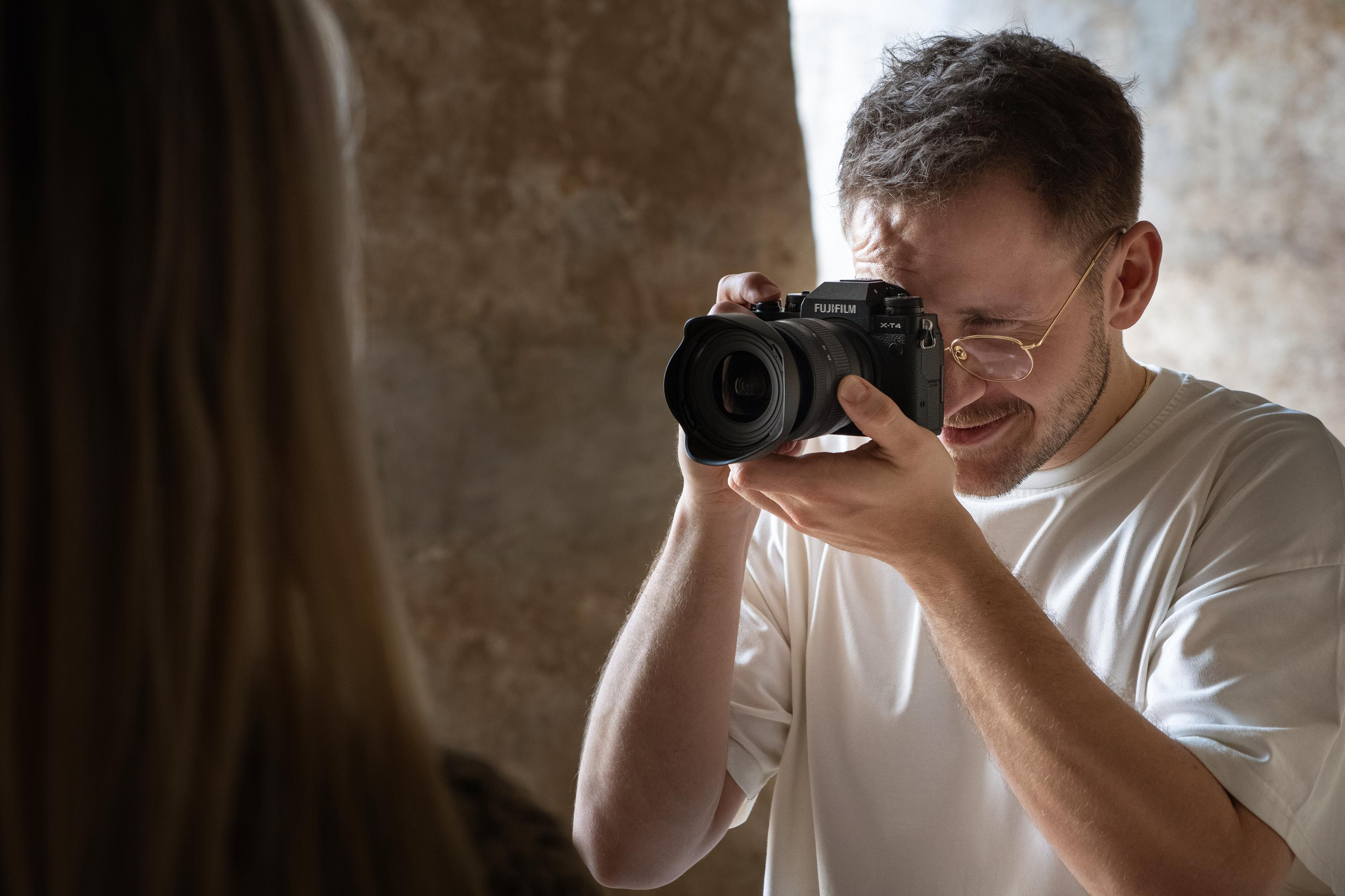 Mężczyzna robi zdjęcie aparatem. Mężczyzna się uśmiecha. Niewyraźna osoba jest w tle.