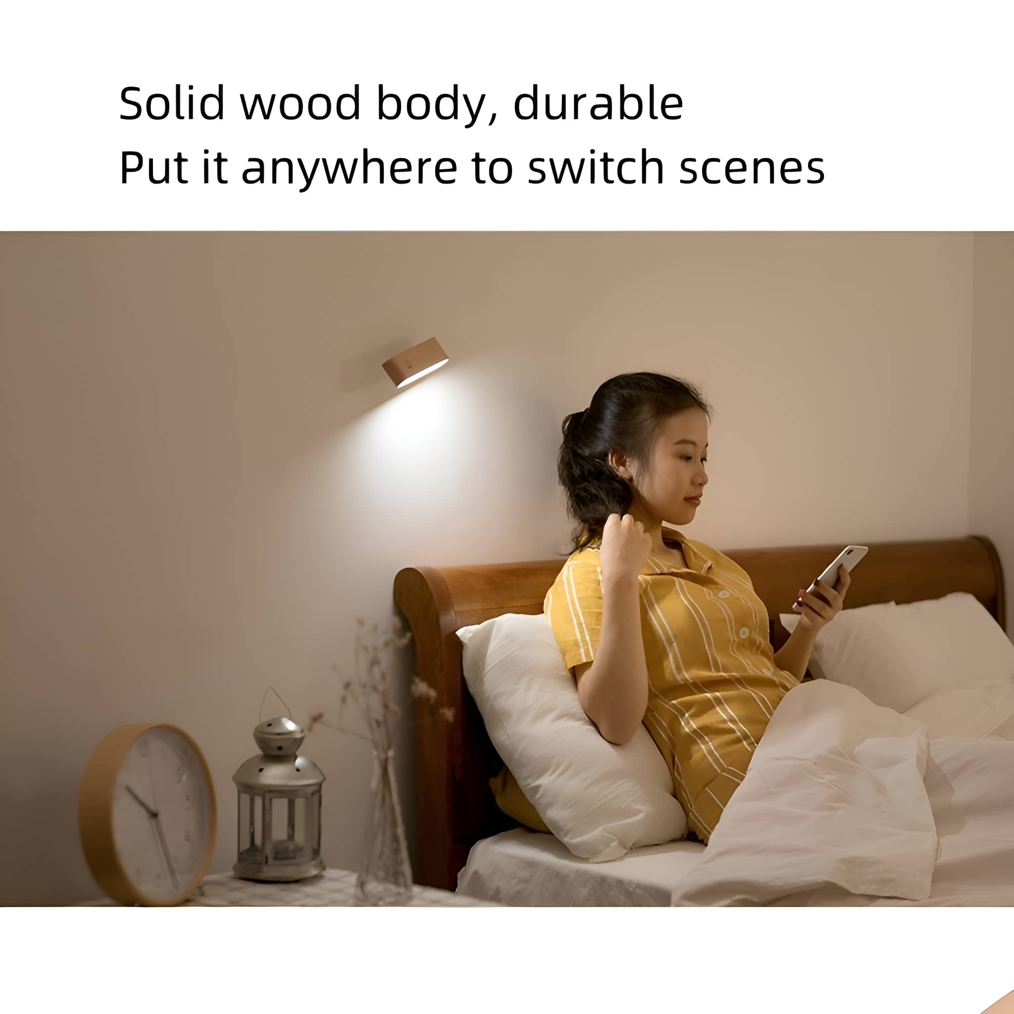 Frau in gelbem Hemd benutzt Handy im Bett. Eine Holzlampe an der Wand und eine Uhr auf dem Nachttisch.