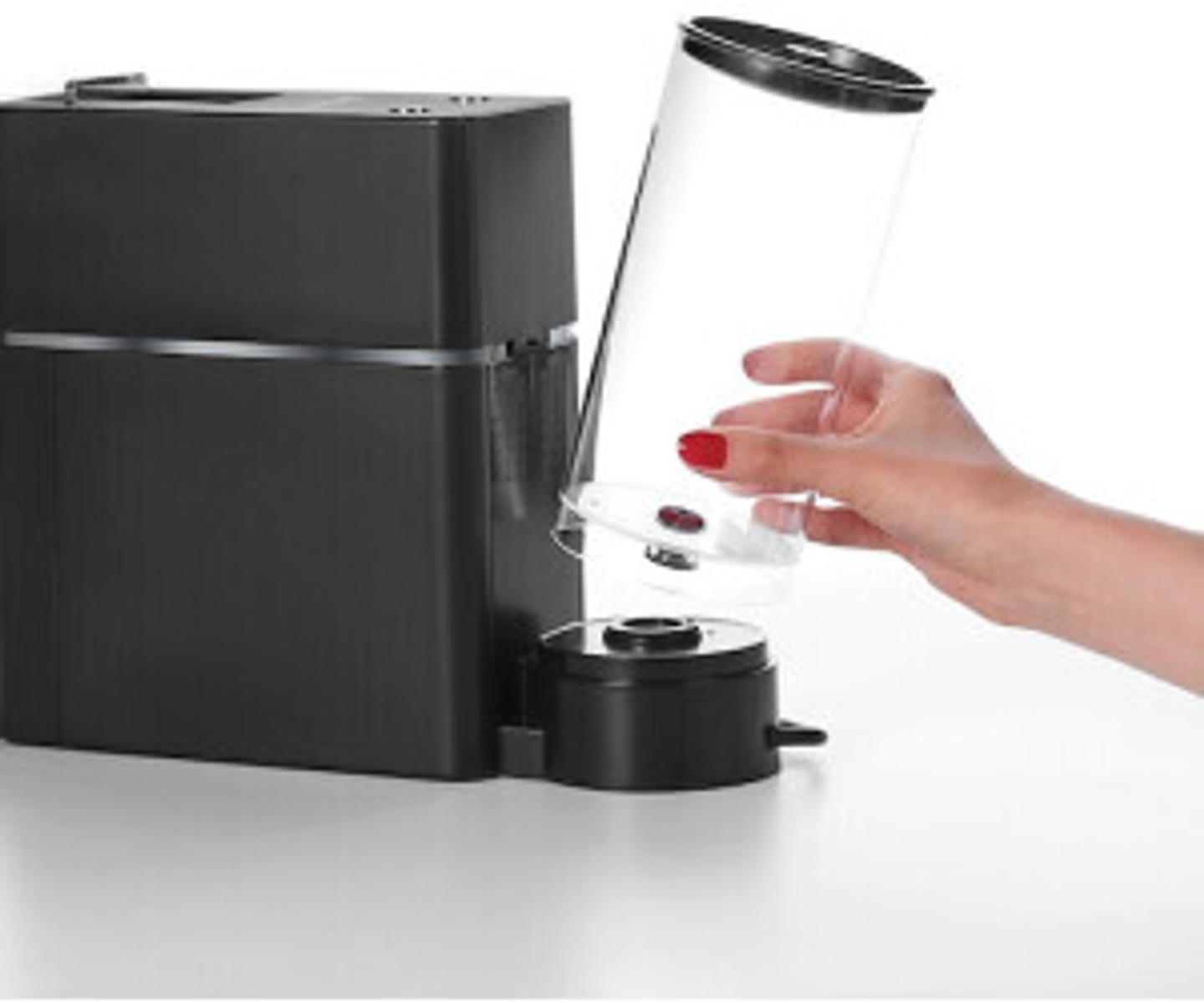 Czarny ekspres do kawy z przezroczystym pojemnikiem trzymanym przez dłoń z czerwonym lakierem do paznokci.