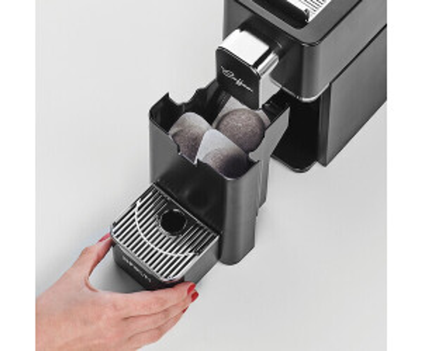 Czarny ekspres do kawy z kapsułkami i ręką umieszczającą tackę. Białe tło.