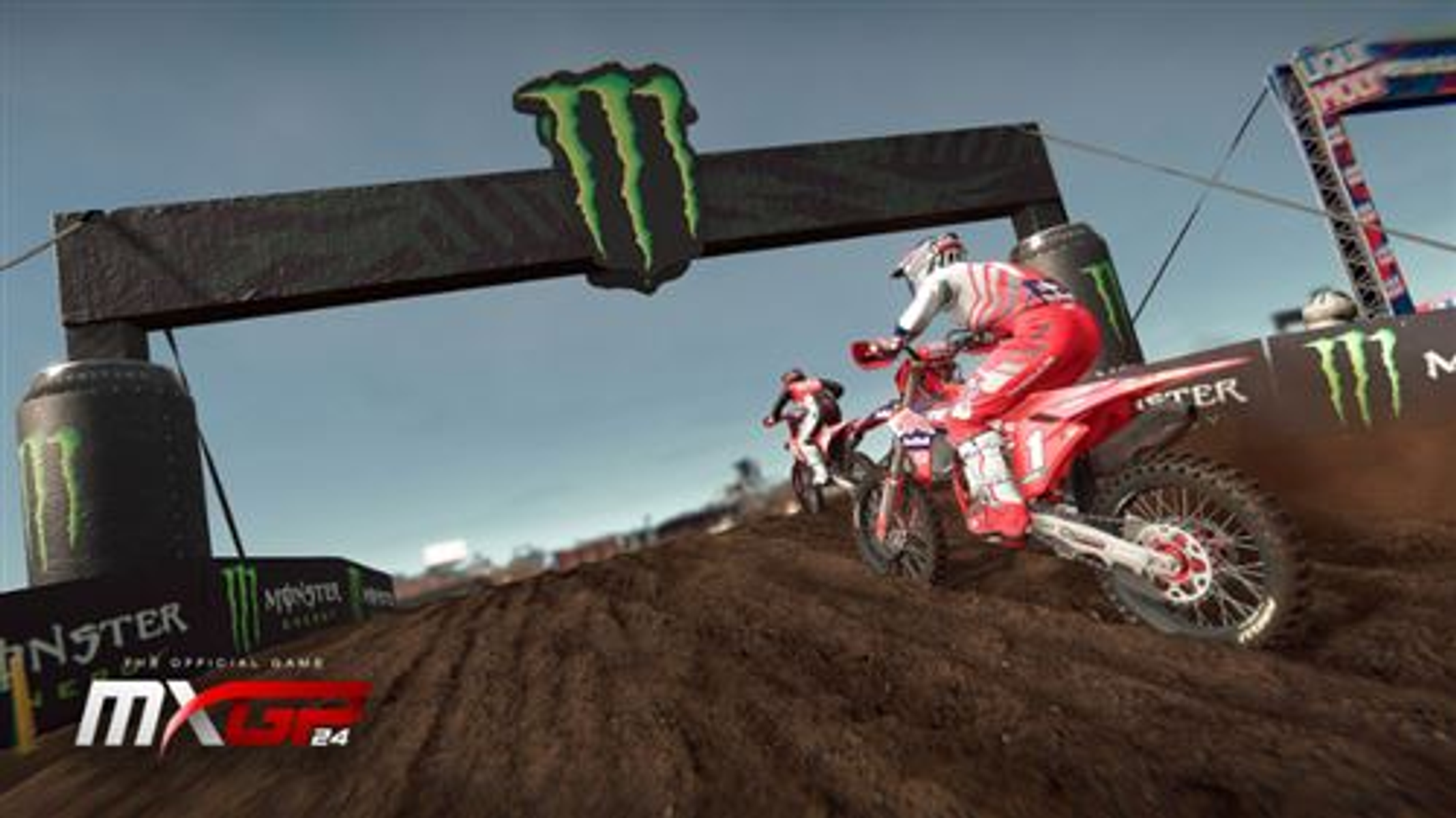 Gara di motocross con piloti su moto da cross, che saltano un dosso, logo Monster Energy visibile.