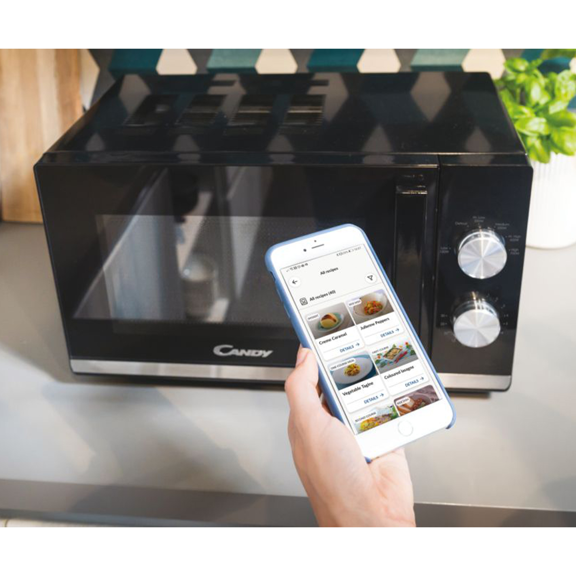 Czarna kuchenka mikrofalowa i dłoń trzymająca telefon z aplikacją z przepisami.