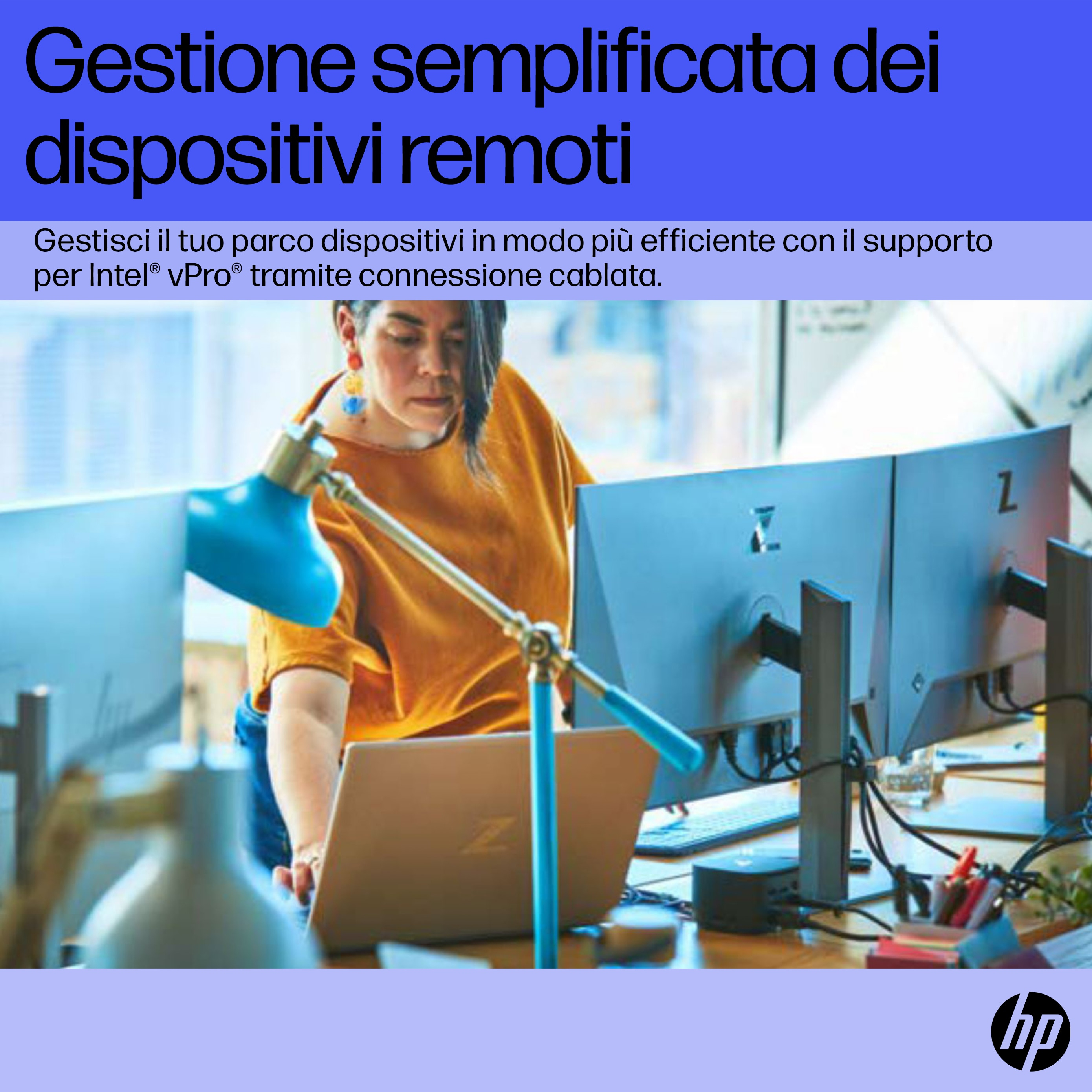 Una donna con un top arancione lavora a una scrivania con monitor e un laptop.