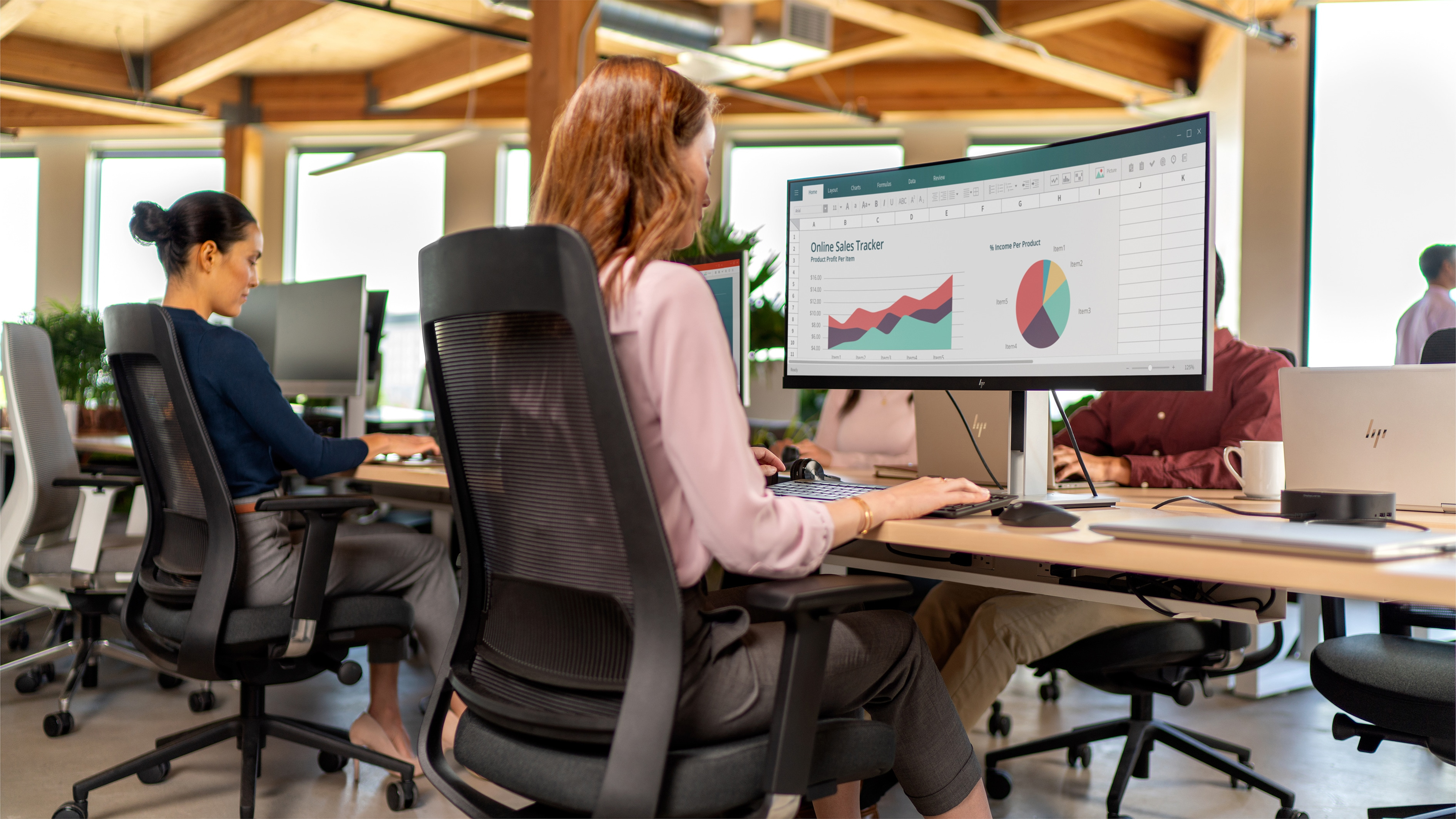 Scena d'ufficio con persone che lavorano su computer e un monitor che mostra grafici.