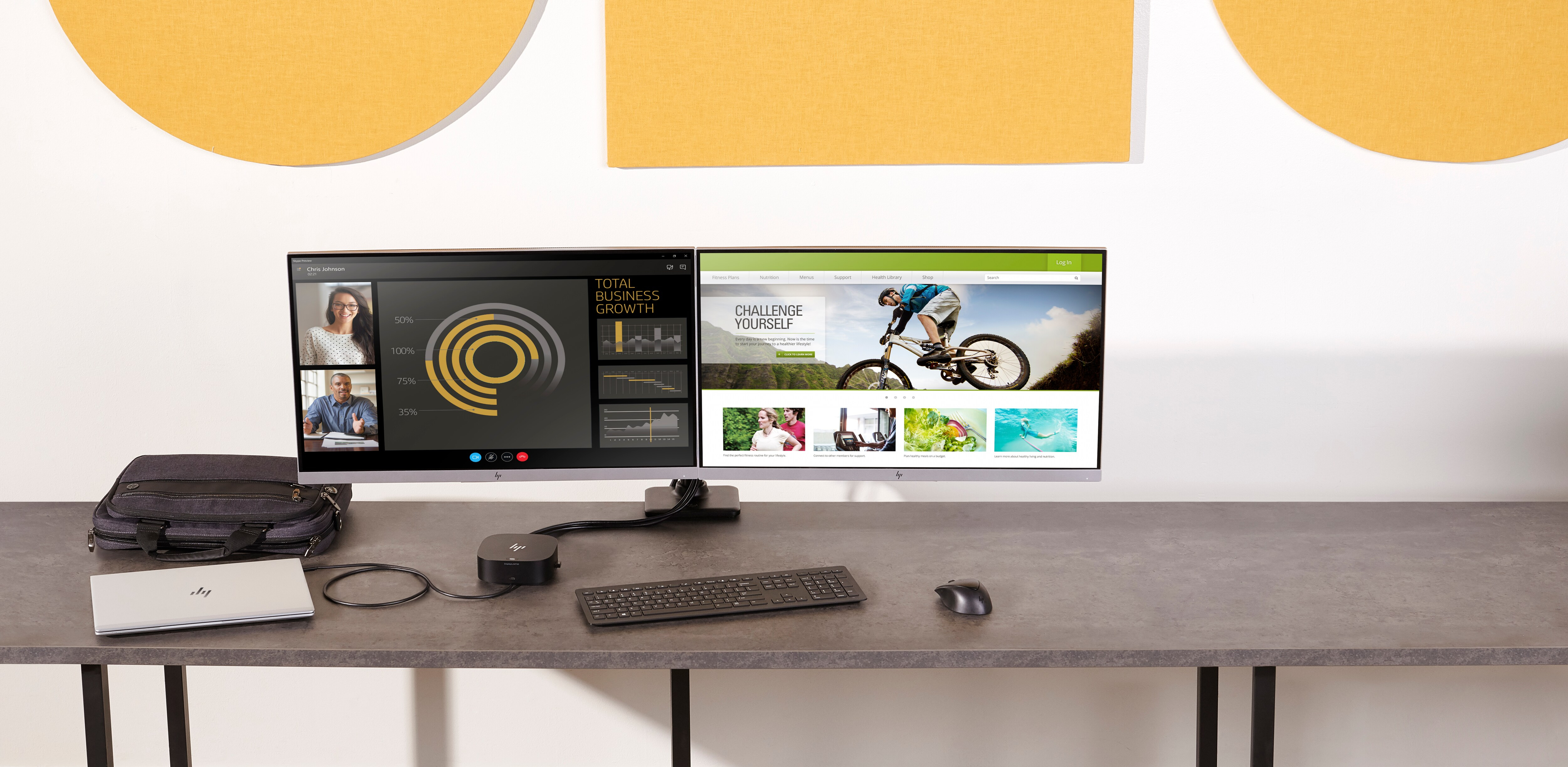 Doppi monitor sulla scrivania con laptop HP e accessori. Decorazioni murali gialle e grigie.