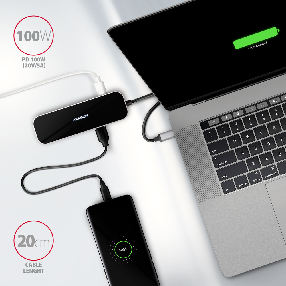 Hub nero, laptop e telefono in carica. L'hub è collegato al laptop. Superficie bianca.