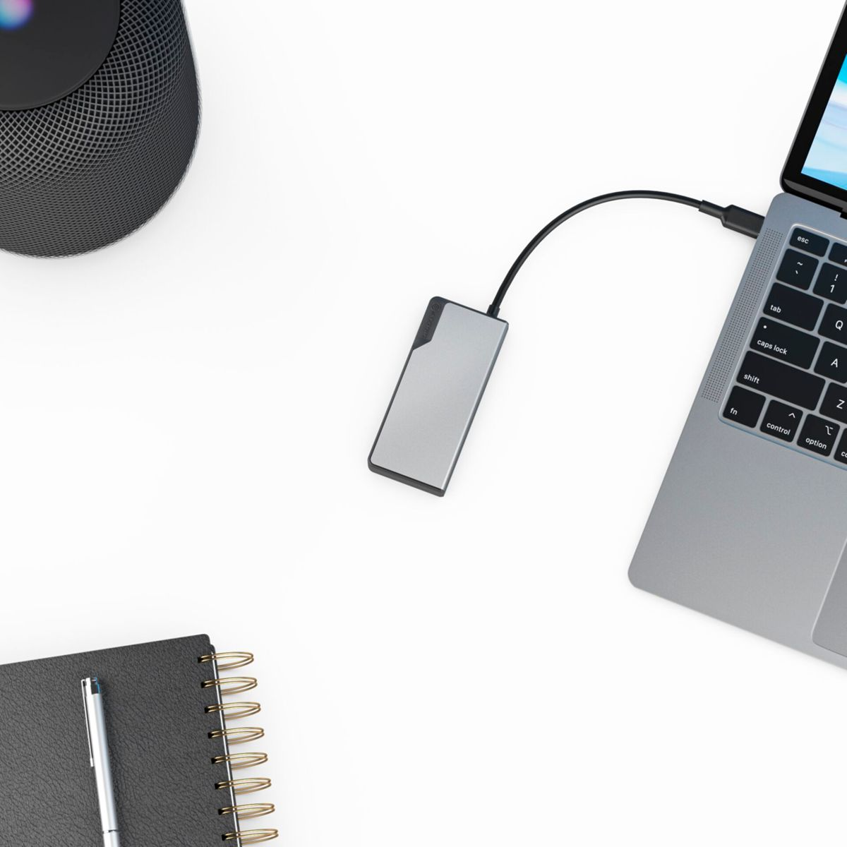 Laptop, con hub USB argentato, accanto a un taccuino nero, penna e altoparlante.