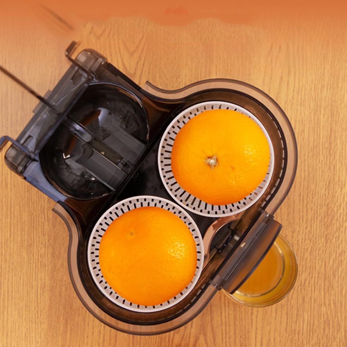Extractor de zumo con dos naranjas en el exprimidor. Un vaso de zumo es visible a la derecha.