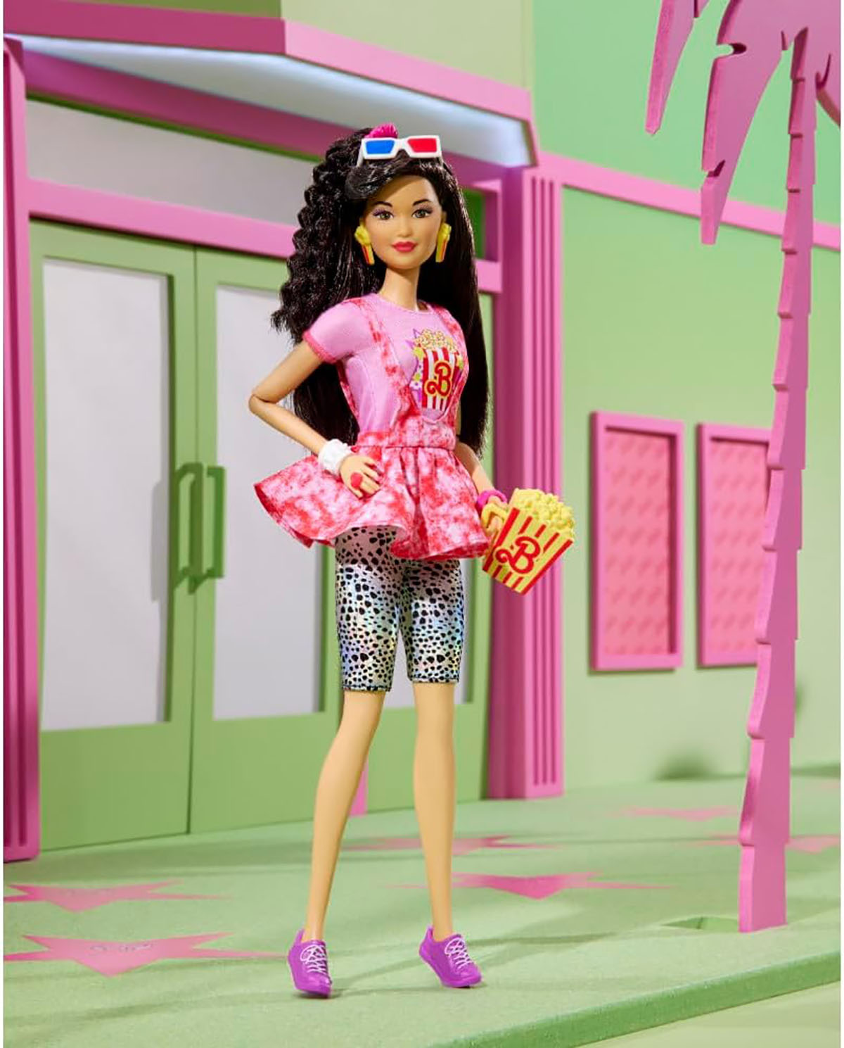 Lalka Barbie w różowej sukience, trzymająca popcorn, z okularami 3D. Zielone i różowe tło.