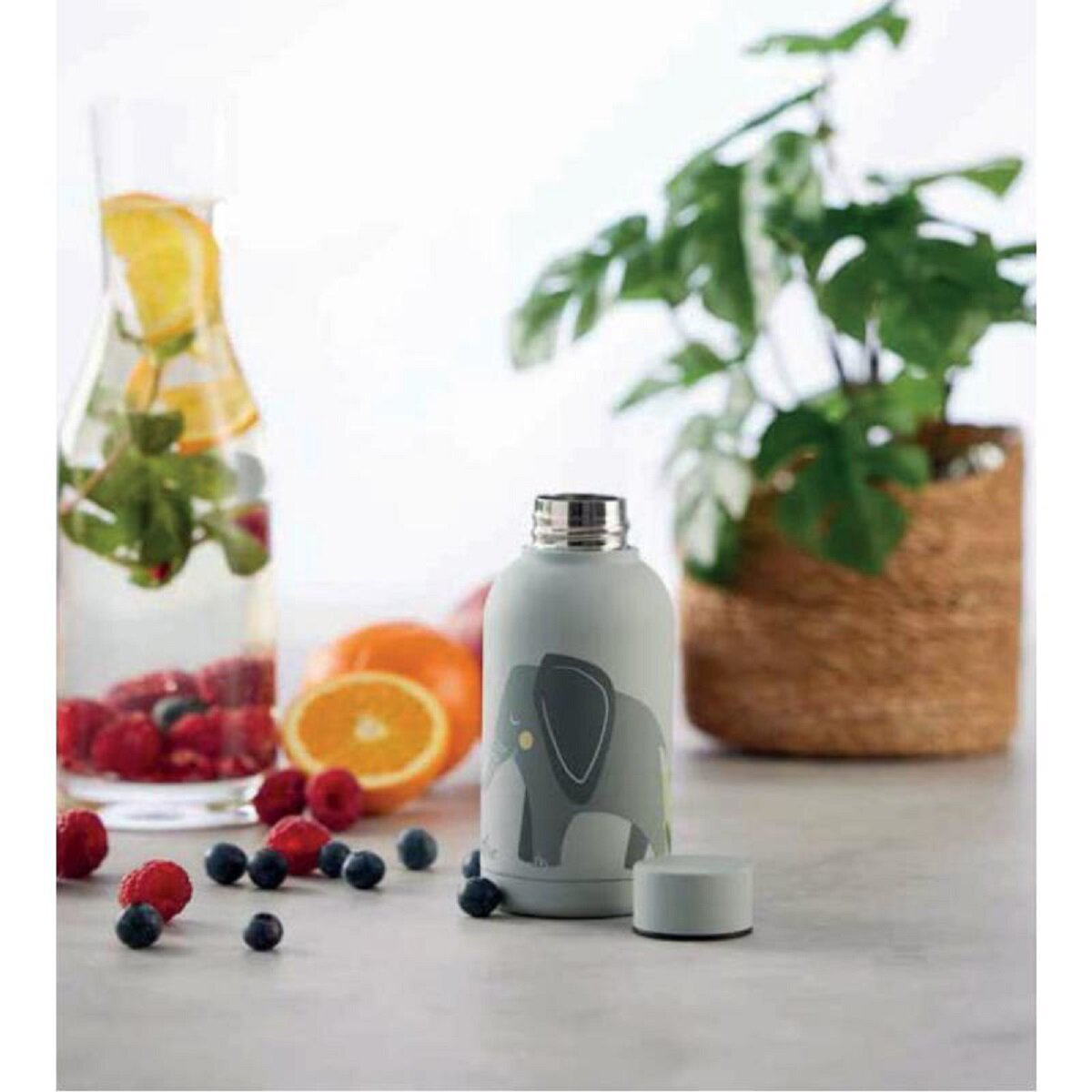 Eine Wasserflasche mit Elefantenmuster, Obst und eine Pflanze in einem Weidenkorb.
