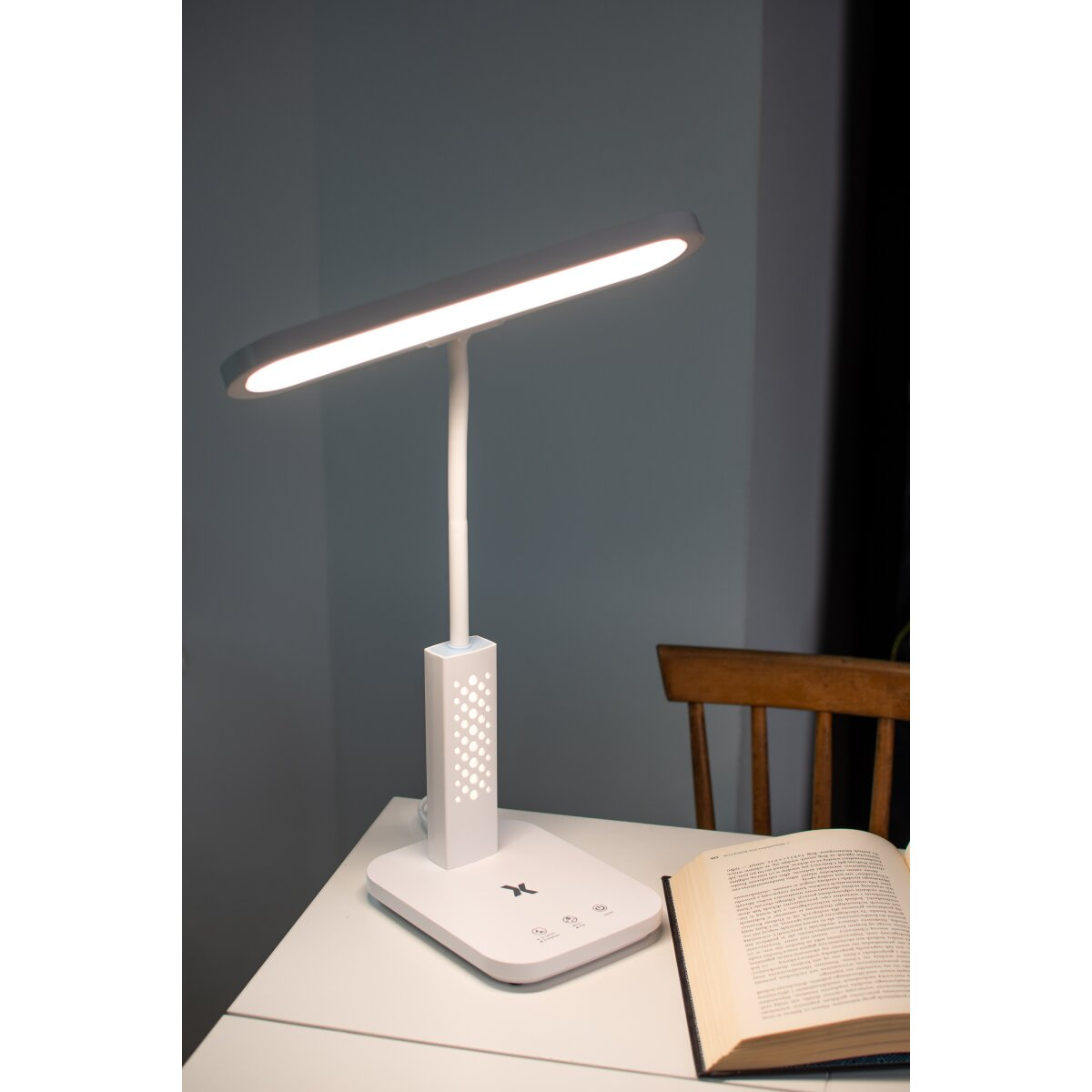 Eine weiße Schreibtischlampe mit einem langen rechteckigen Licht, einem Ständer und einem Buch auf dem Schreibtisch.
