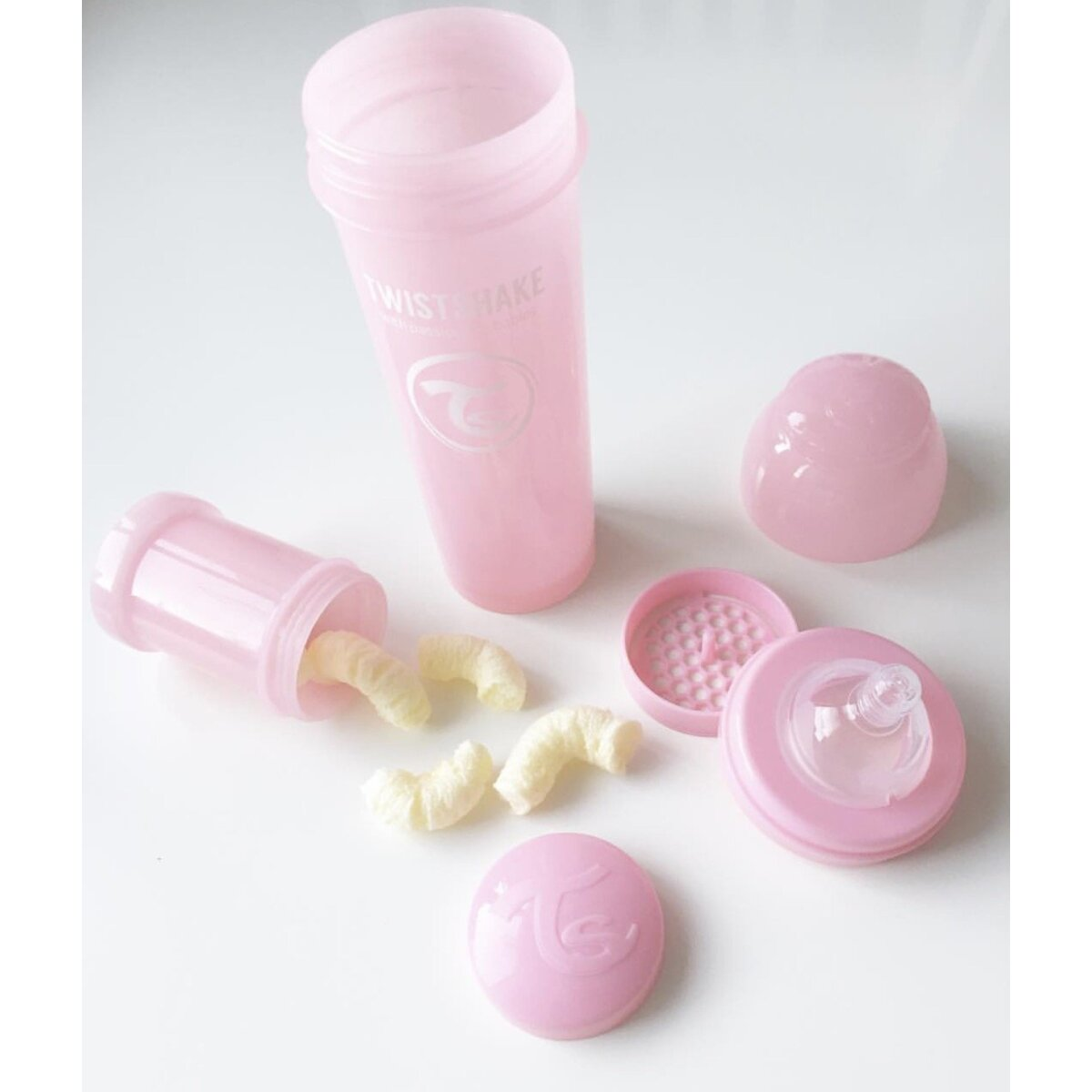 Rosa Babyflaschenteile, einschließlich Flasche, Deckel und Snacks, auf weißem Hintergrund.