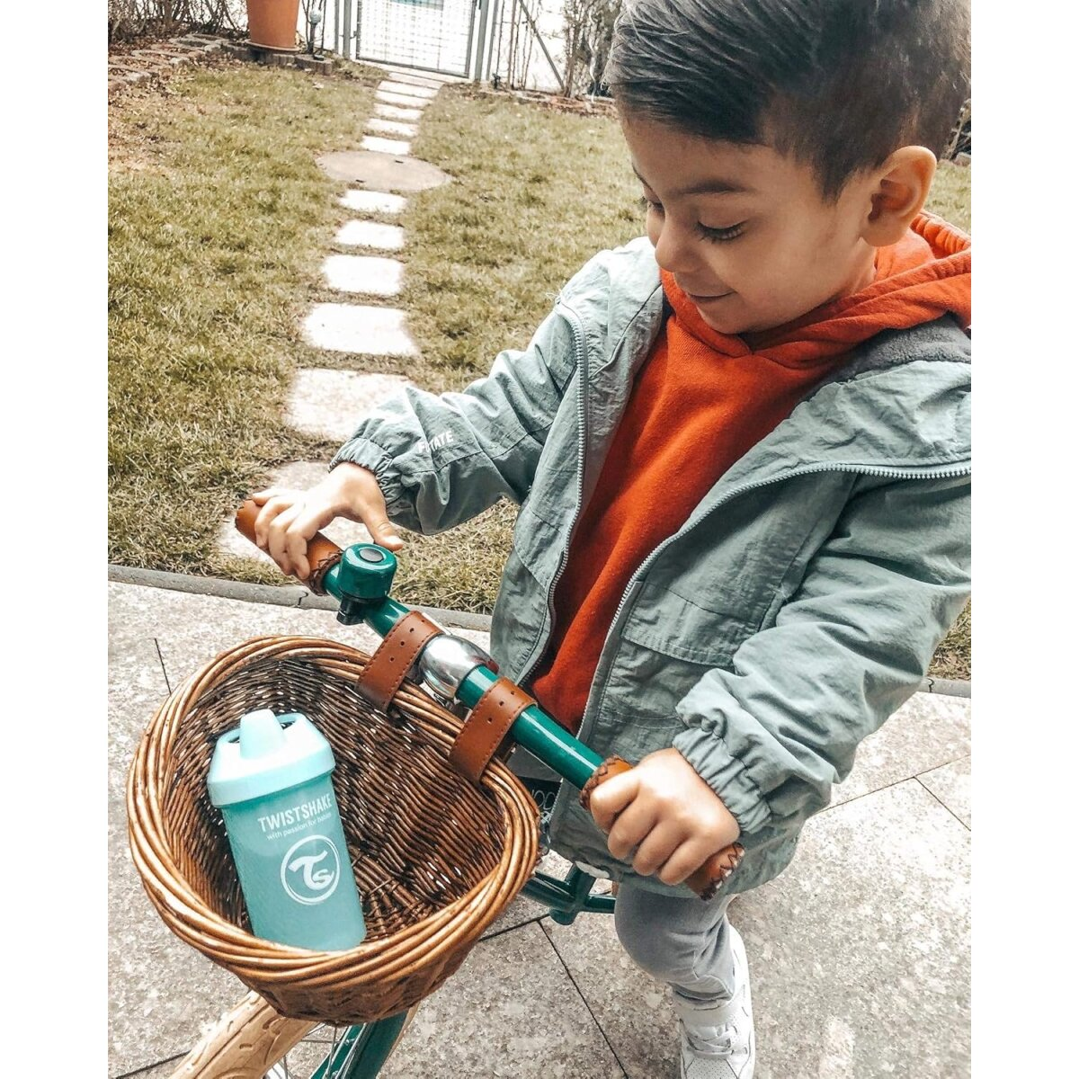 Junger Junge auf einem Fahrrad, hält Lenker mit einem Korb mit einer Flasche, auf einem grasbewachsenen Weg.