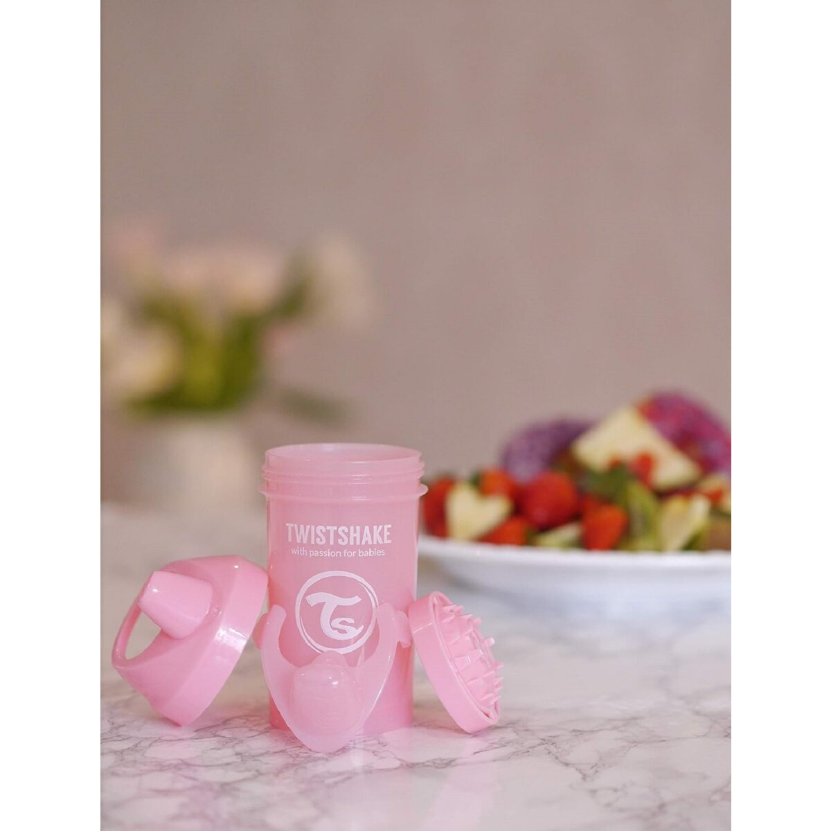 Pinke Twistshake-Flasche mit Deckel und Obstsalat im Hintergrund.