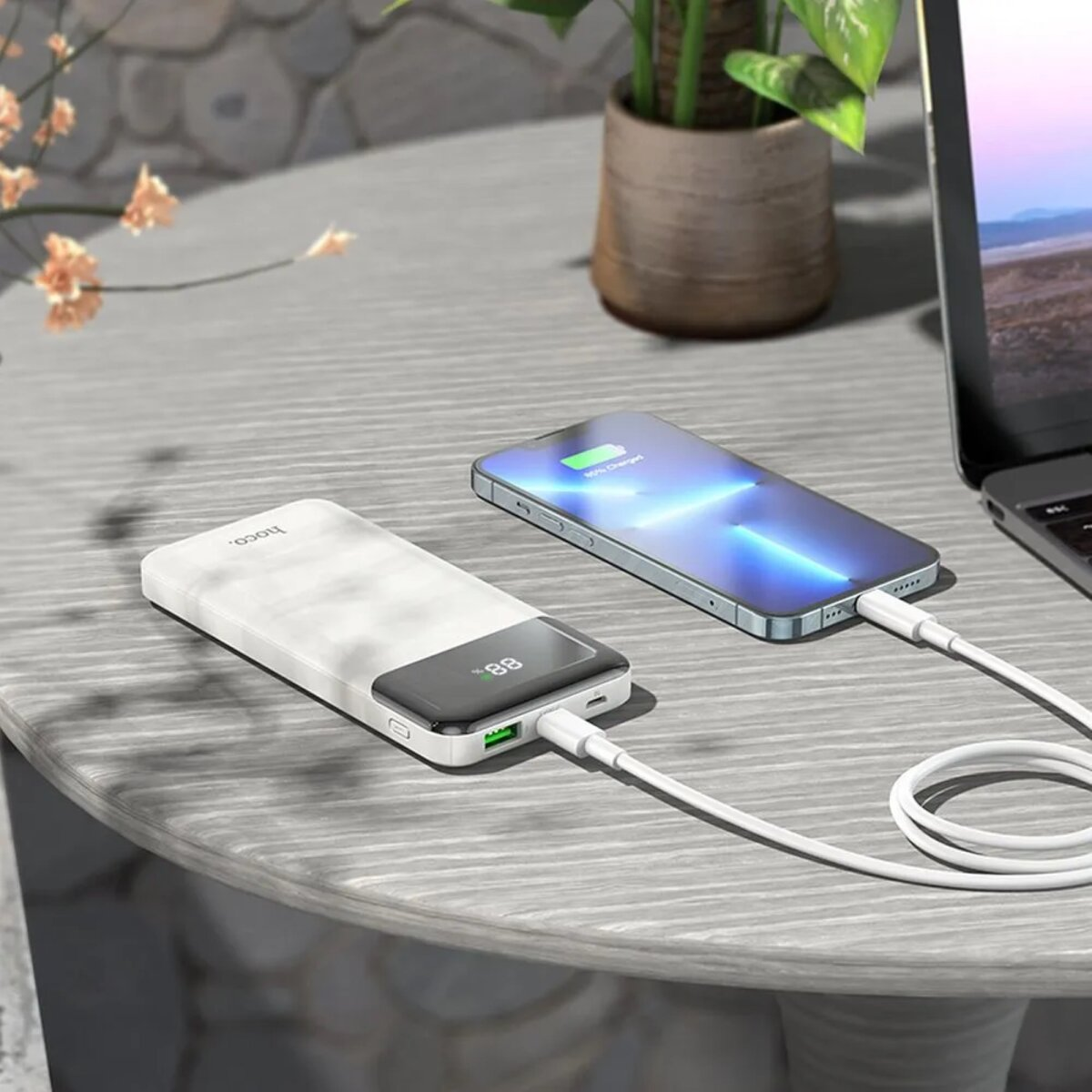 Zwei Handys laden. Eine weiße Powerbank, ein Telefon, ein Kabel auf einem Holztisch.