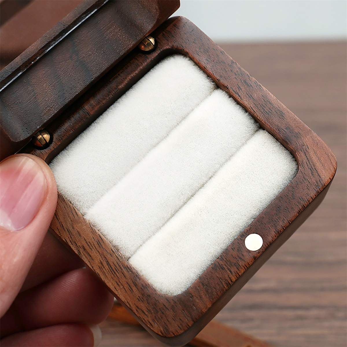 Geöffnete Holzringbox. Innen hält weißer Samt Ringe. Goldene Scharniere und ein goldener Punktverschluss sichtbar.