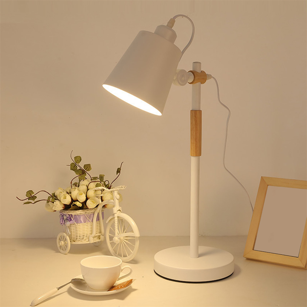 Eine weiße Schreibtischlampe mit Holzakzent, ein kleiner fahrradförmiger Blumenhalter und ein Bilderrahmen.