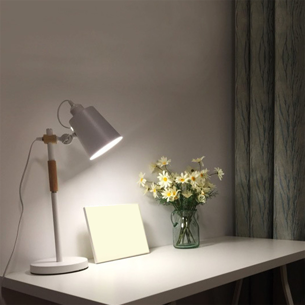 Eine Schreibtischlampe, eine Vase mit Blumen und eine weiße Oberfläche mit quadratischem Rahmen.