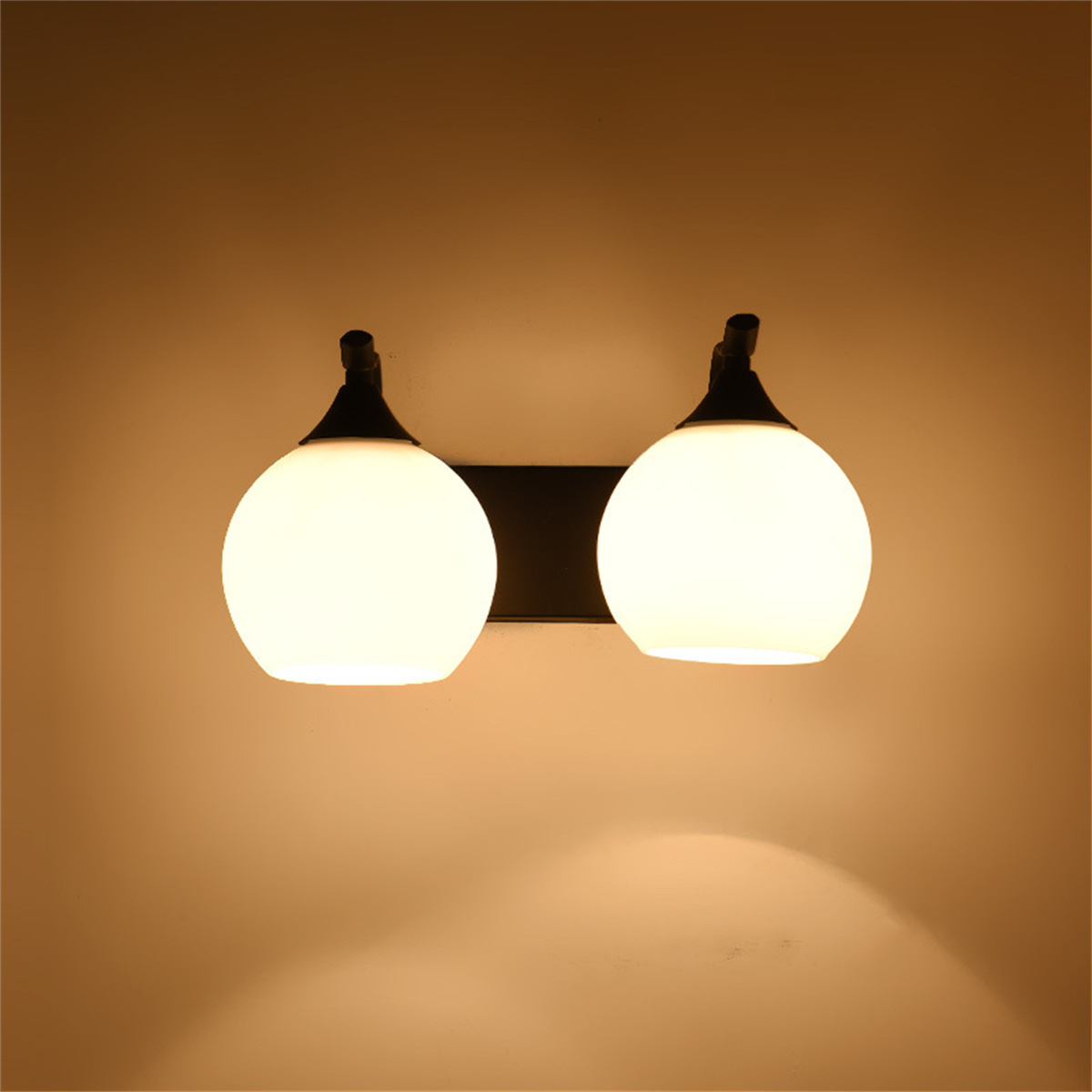 Zwei weiße, kugelförmige Wandleuchten an einer schwarzen Stange, an einer beigen Wand. Die Lichter sind an.