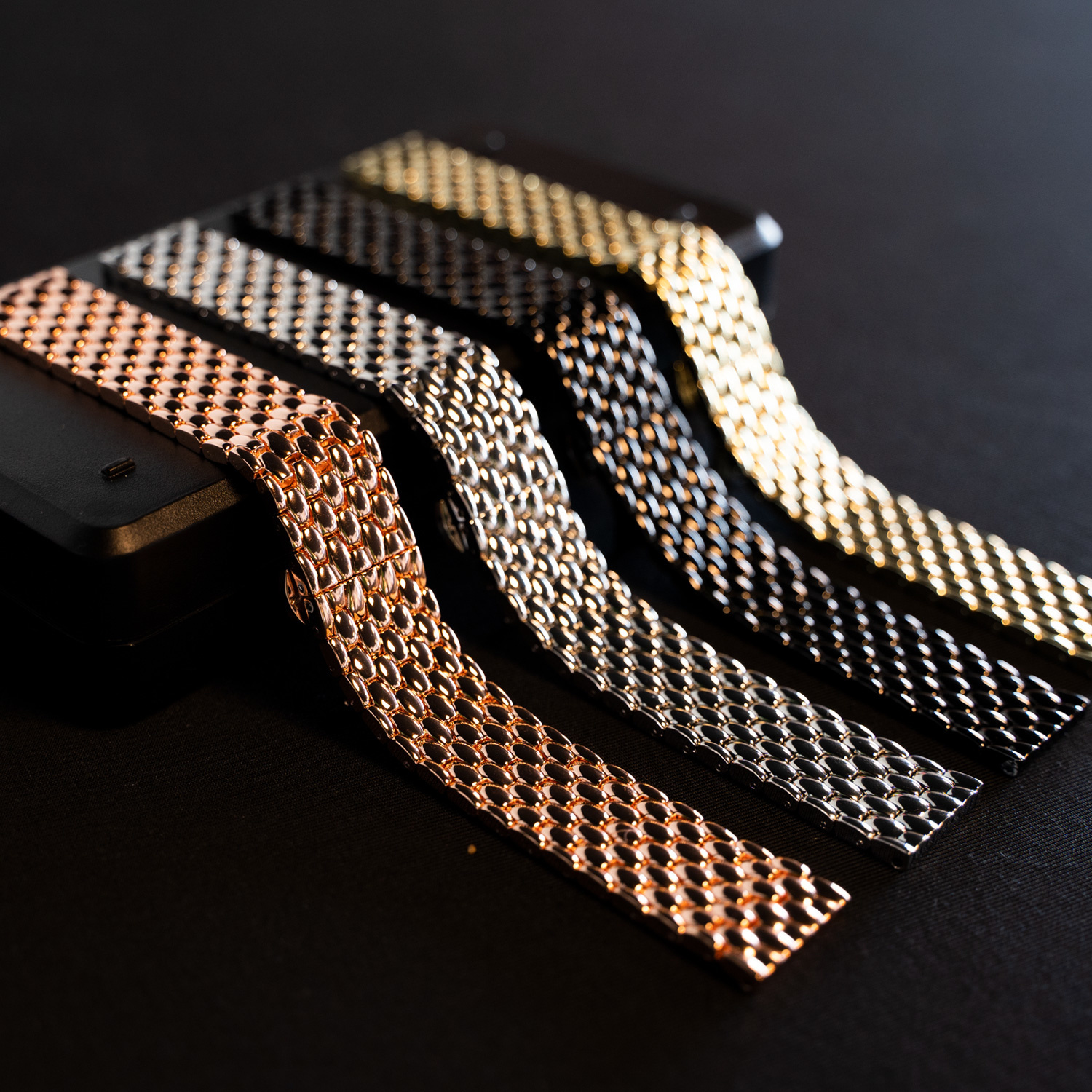Vier Metall-Uhrenarmbänder in verschiedenen Farben: Roségold, Silber, Schwarz und Gold.