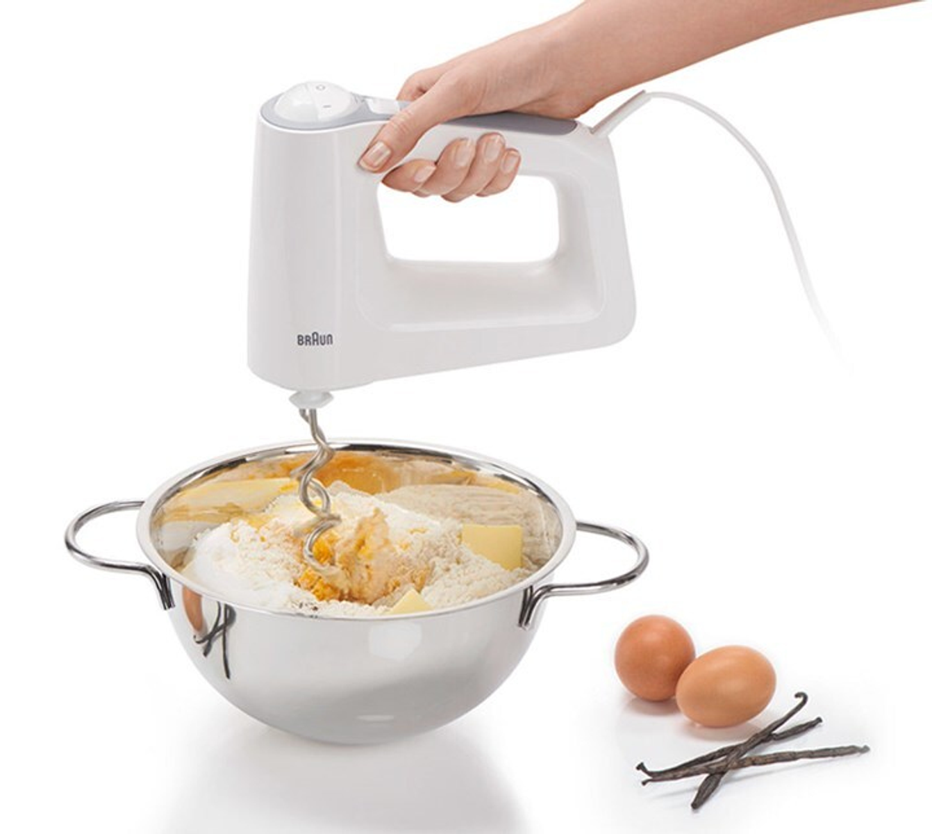 Een persoon die een witte handmixer gebruikt om ingrediënten in een metalen kom te mengen.