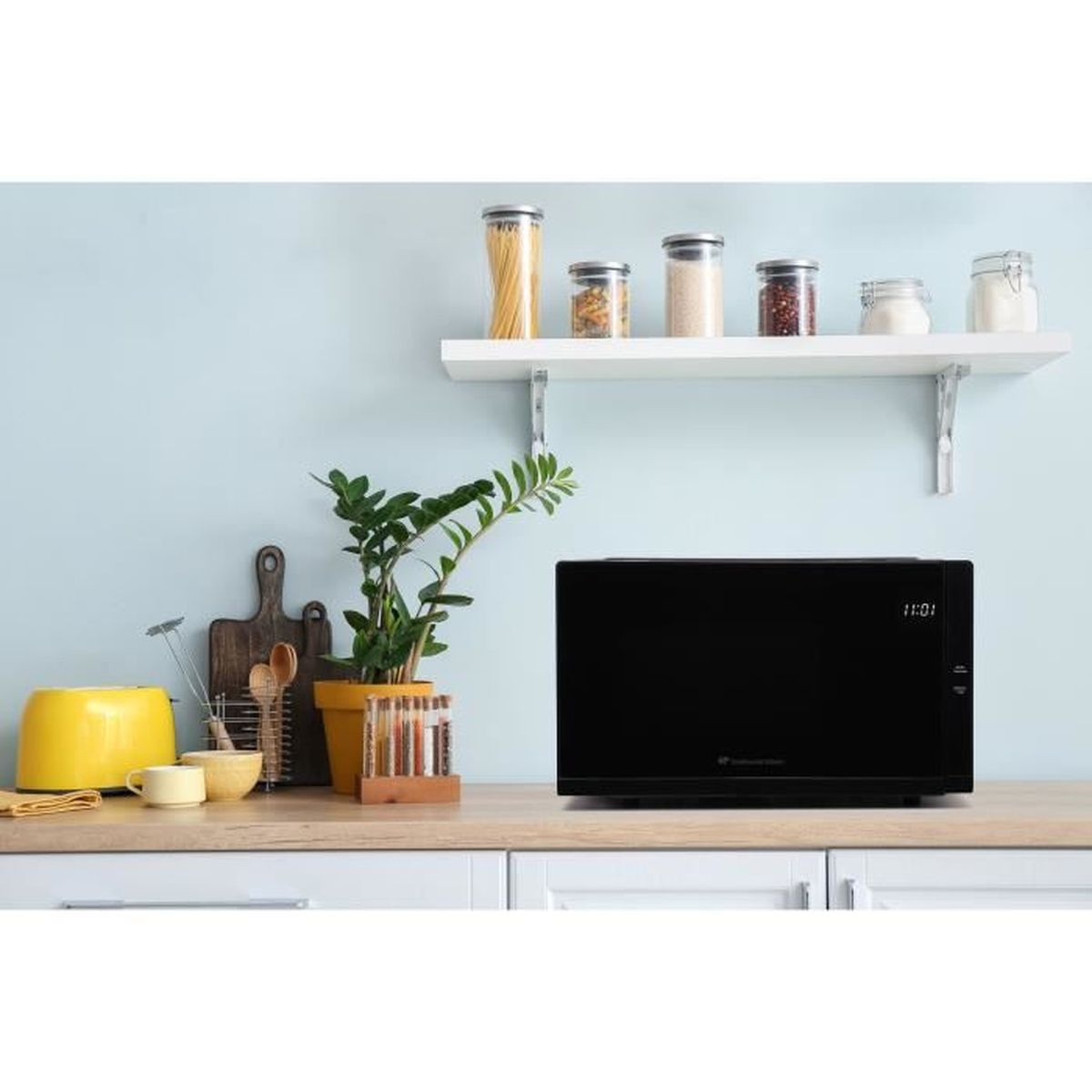 Encimera de cocina con microondas, planta y frascos. Pared azul al fondo.