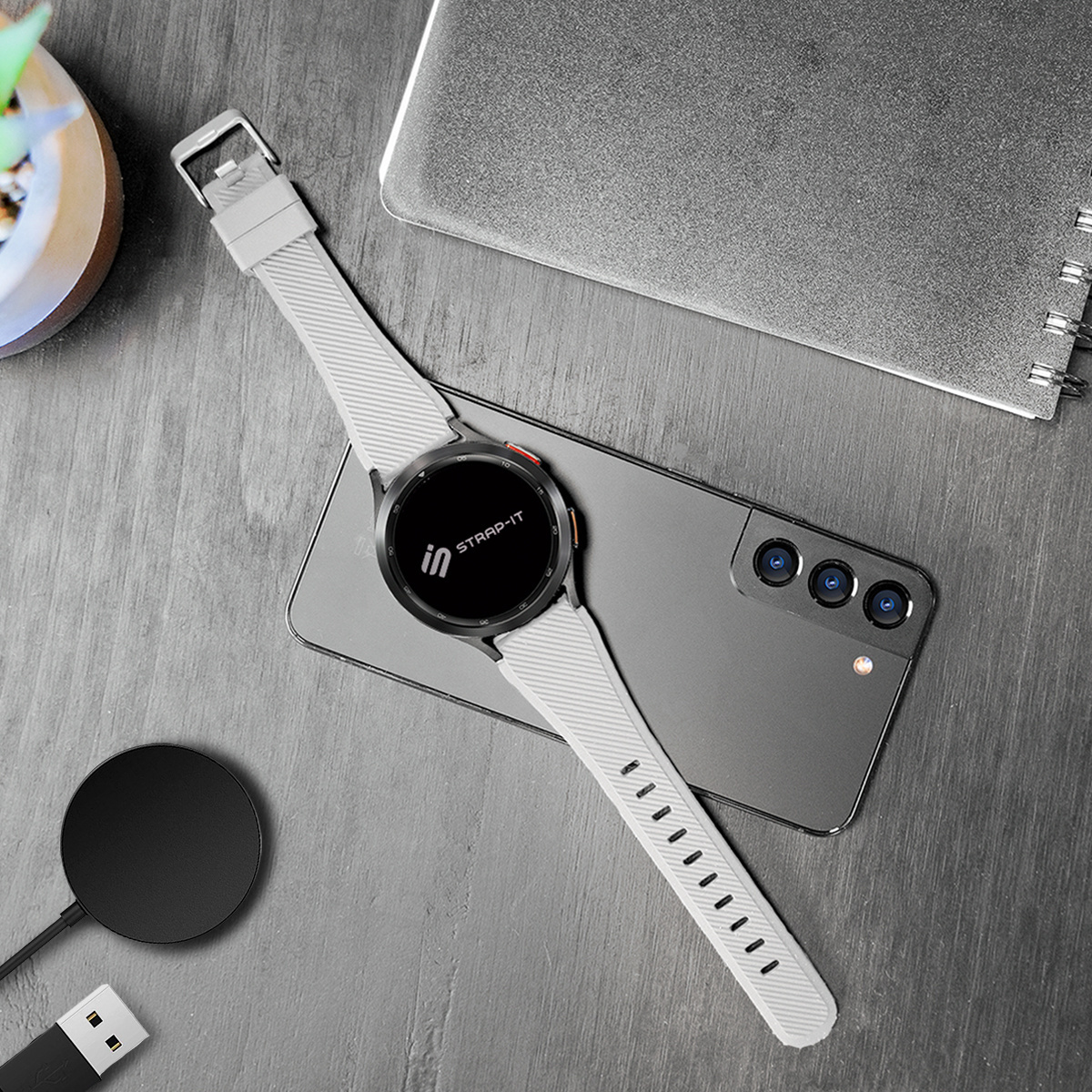 Eine Smartwatch und ein Smartphone auf einem Schreibtisch. Ein Ladegerät und ein Notizbuch sind ebenfalls vorhanden.