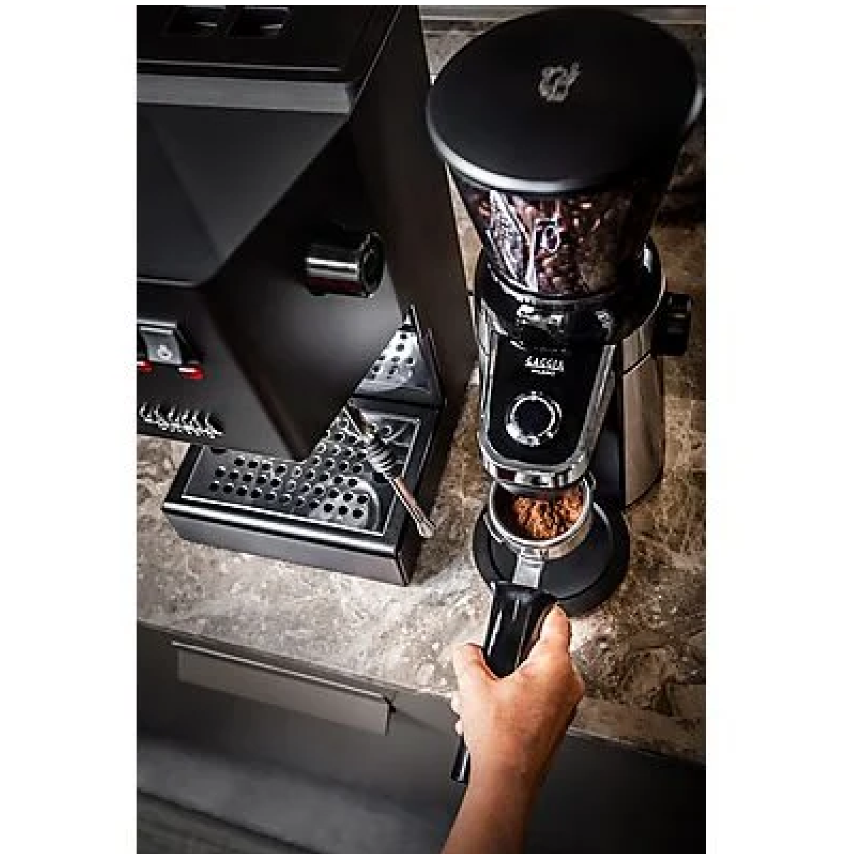 Młynek do kawy z ziarnami w górnej komorze i kawą w dolnym uchwycie. Ręka trzyma uchwyt.