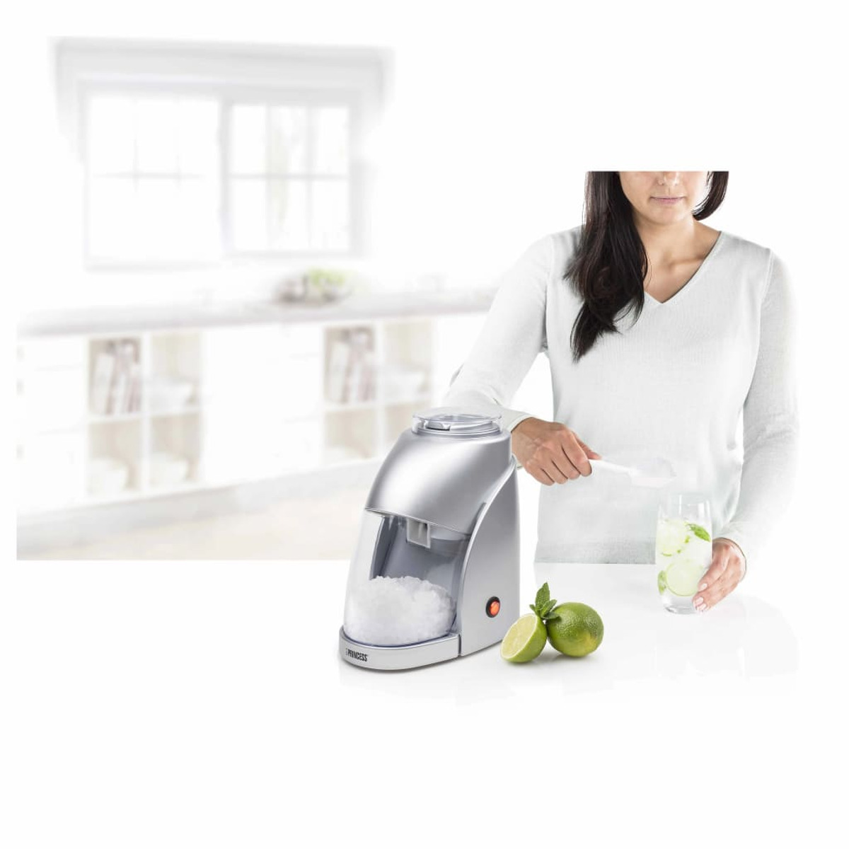 Eine Frau benutzt eine Eismaschine. Auf dem Tisch stehen ein Glas mit Limetten und Eis.