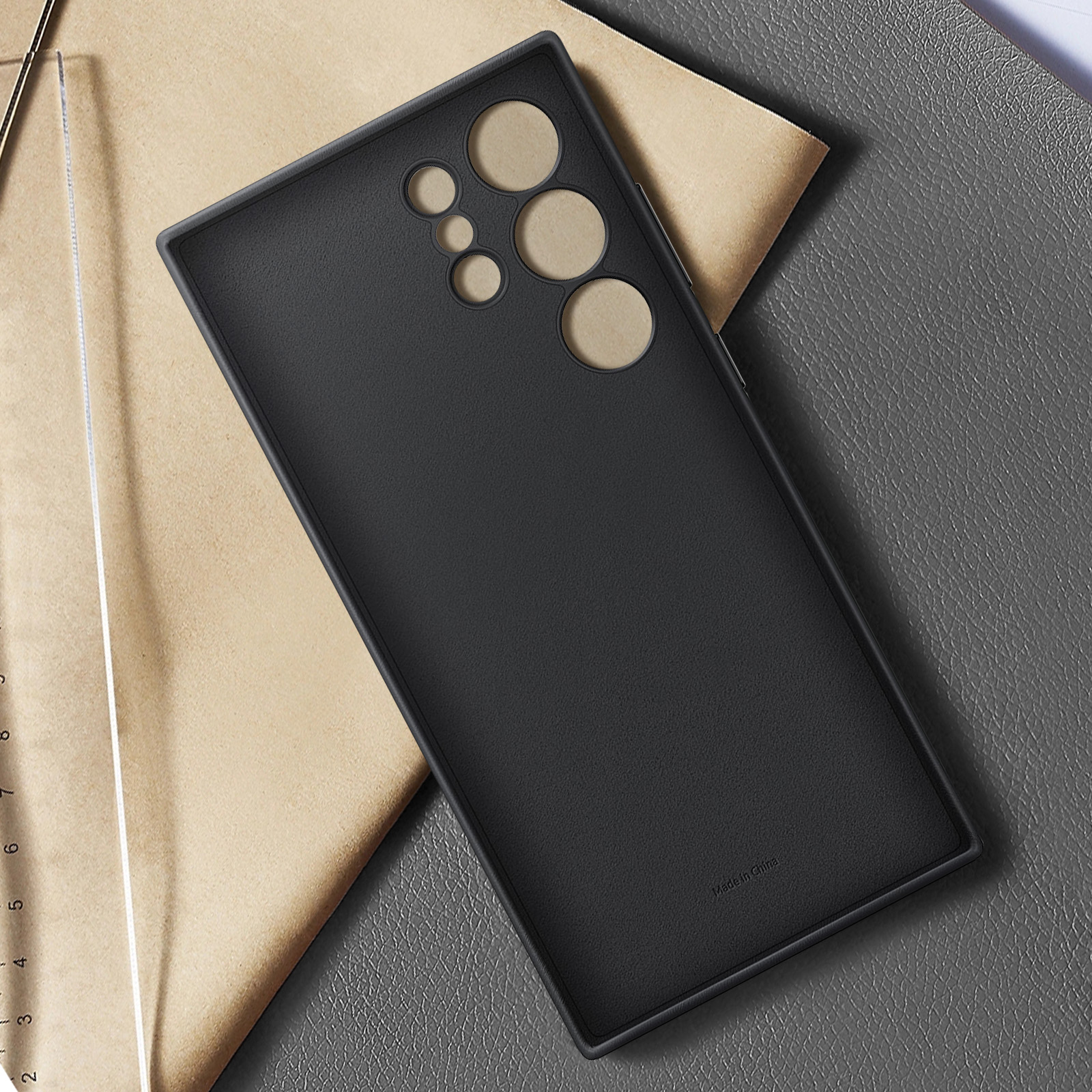 Zwarte telefoonhoes met een gladde textuur. Hoesje heeft camera-uitsparingen en ligt op een grijs oppervlak.