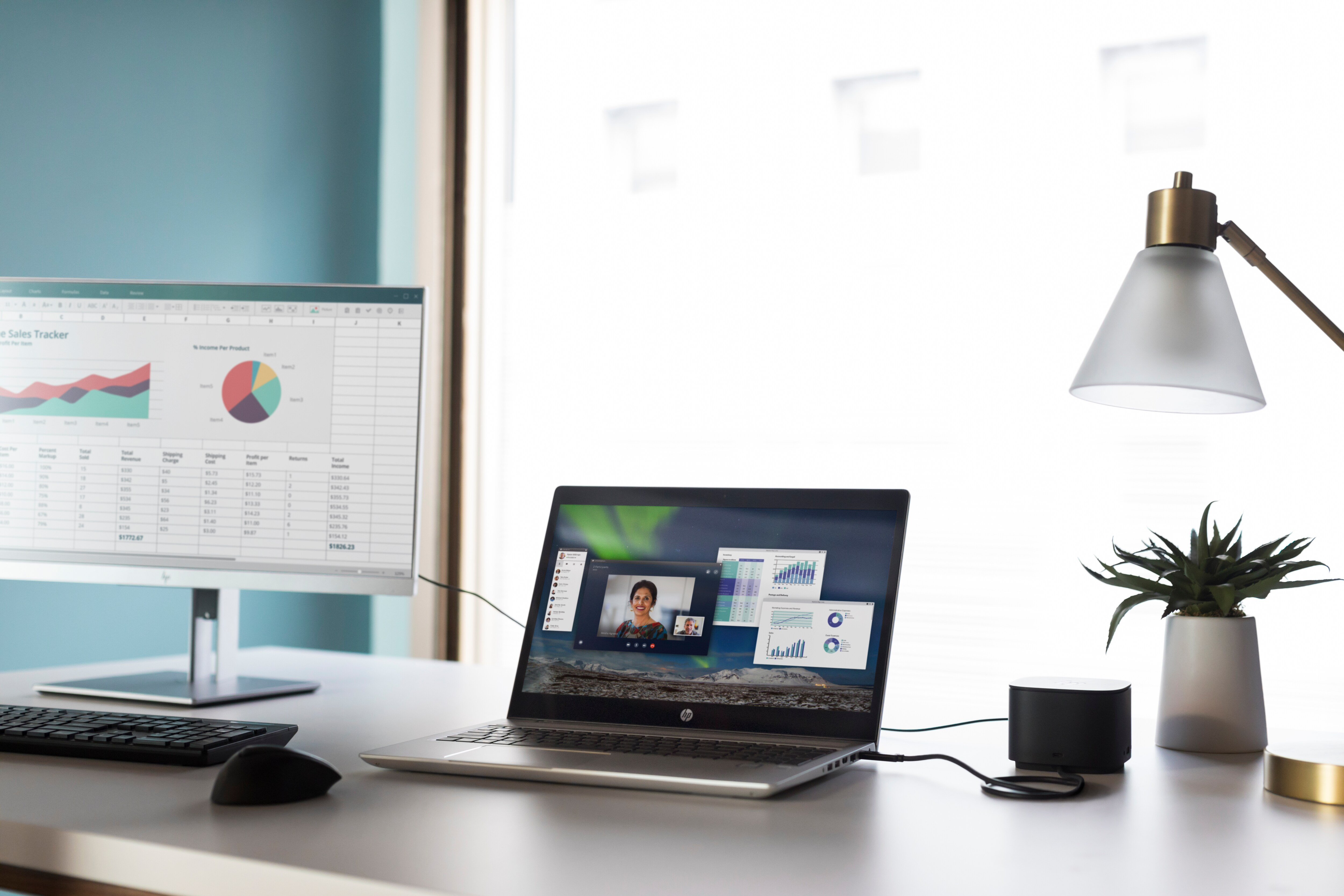 Konfiguracja biurka z laptopem, monitorem i małym głośnikiem. Na ekranie laptopa jest rozmowa wideo.