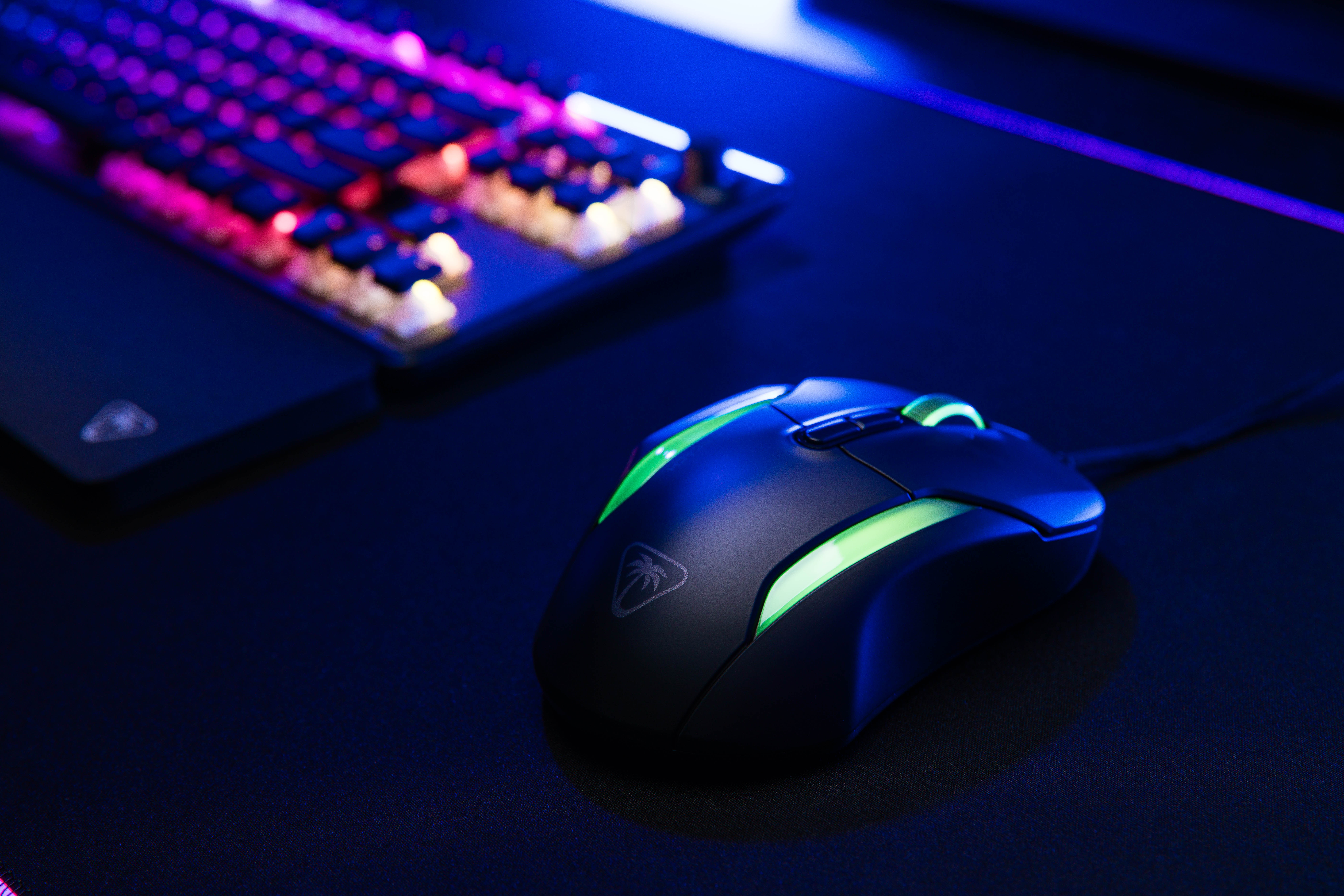 Mysz do gier na czarnej powierzchni, podświetlana na zielono. Klawiatura w tle.