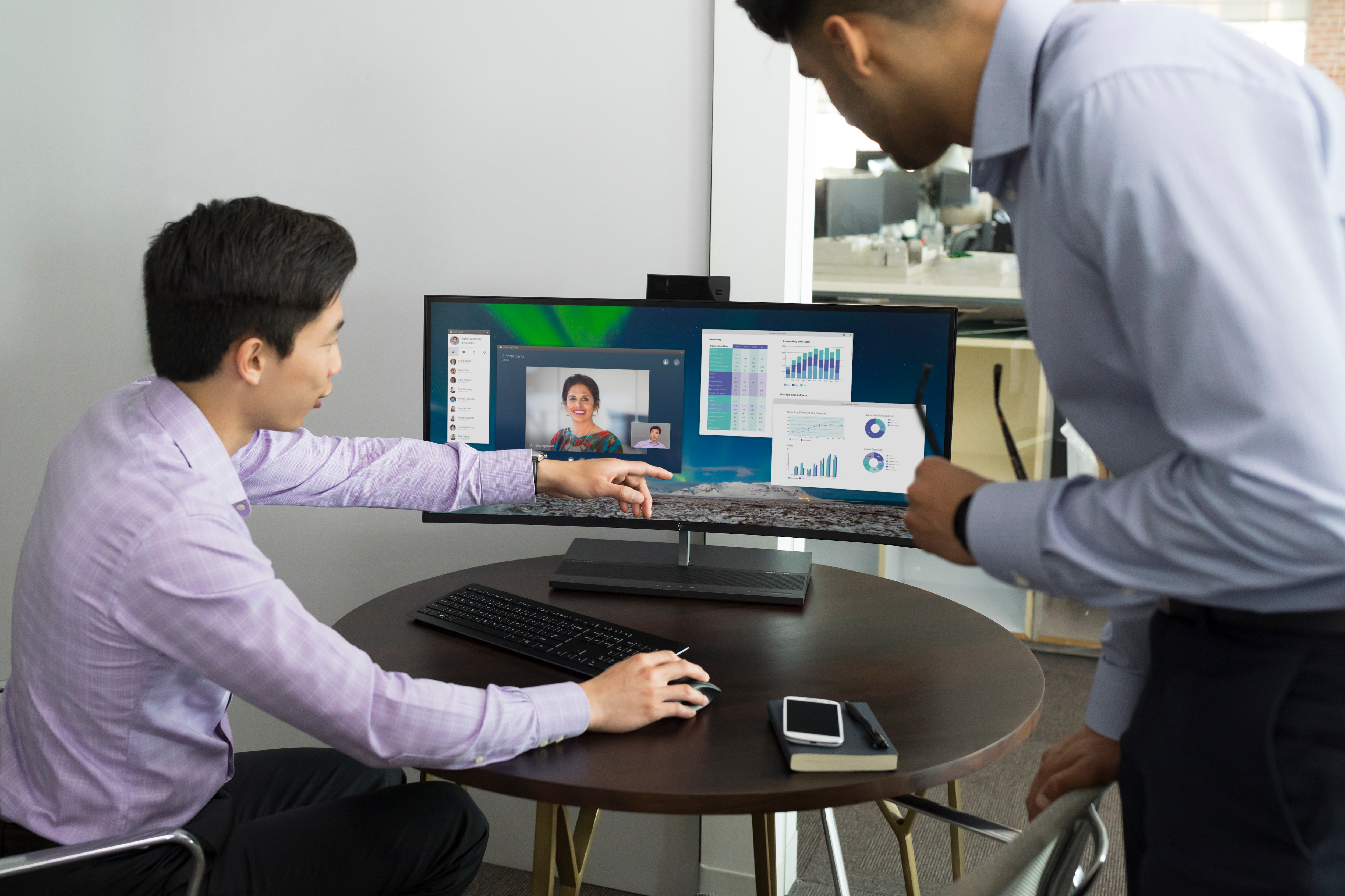Dwóch mężczyzn oglądających ekran komputera podczas rozmowy wideo, z widocznymi wykresami.
