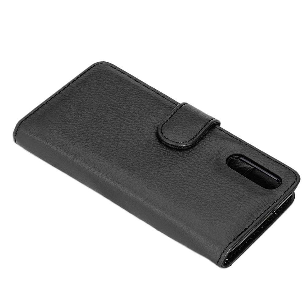 Una custodia per telefono in pelle nera chiusa con chiusura magnetica, angolata su una superficie bianca. Focus sulla custodia.