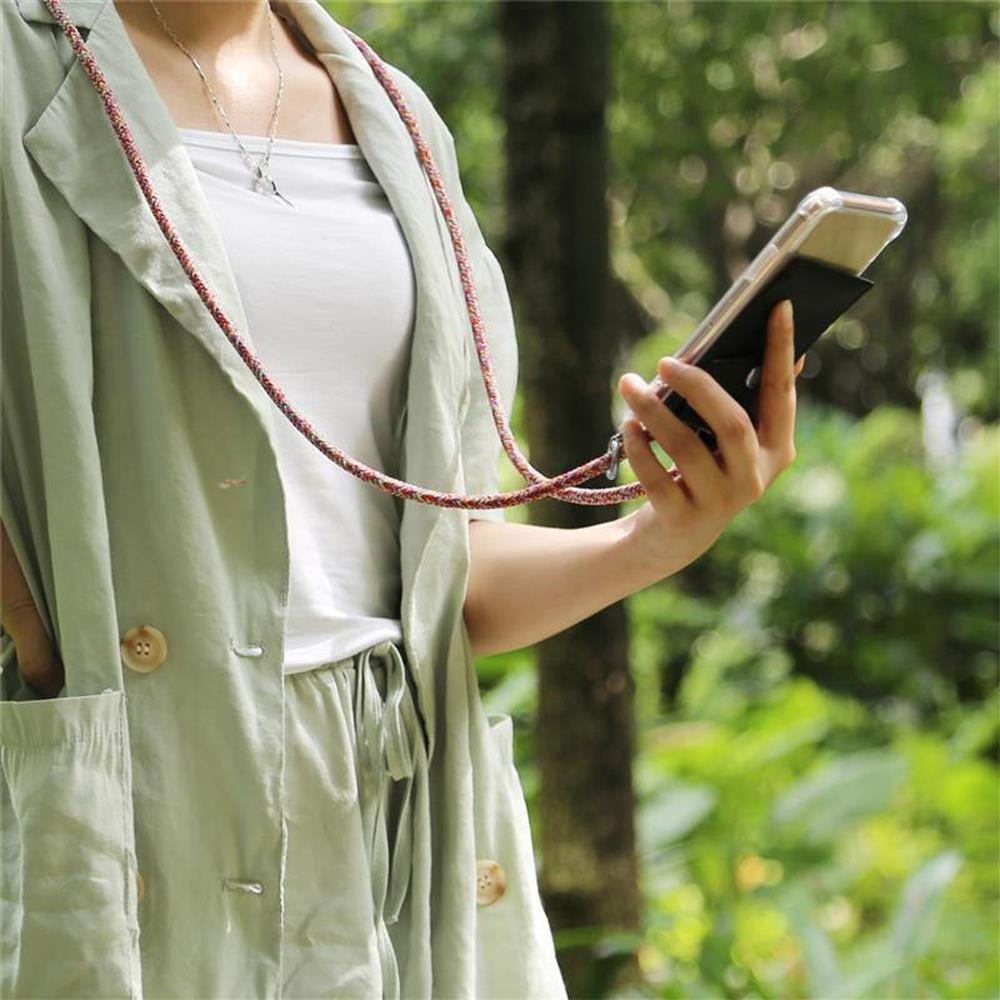 Eine Person in einer grünen Jacke hält ein Telefon mit einem Schlüsselband. Der Hintergrund ist unscharf.